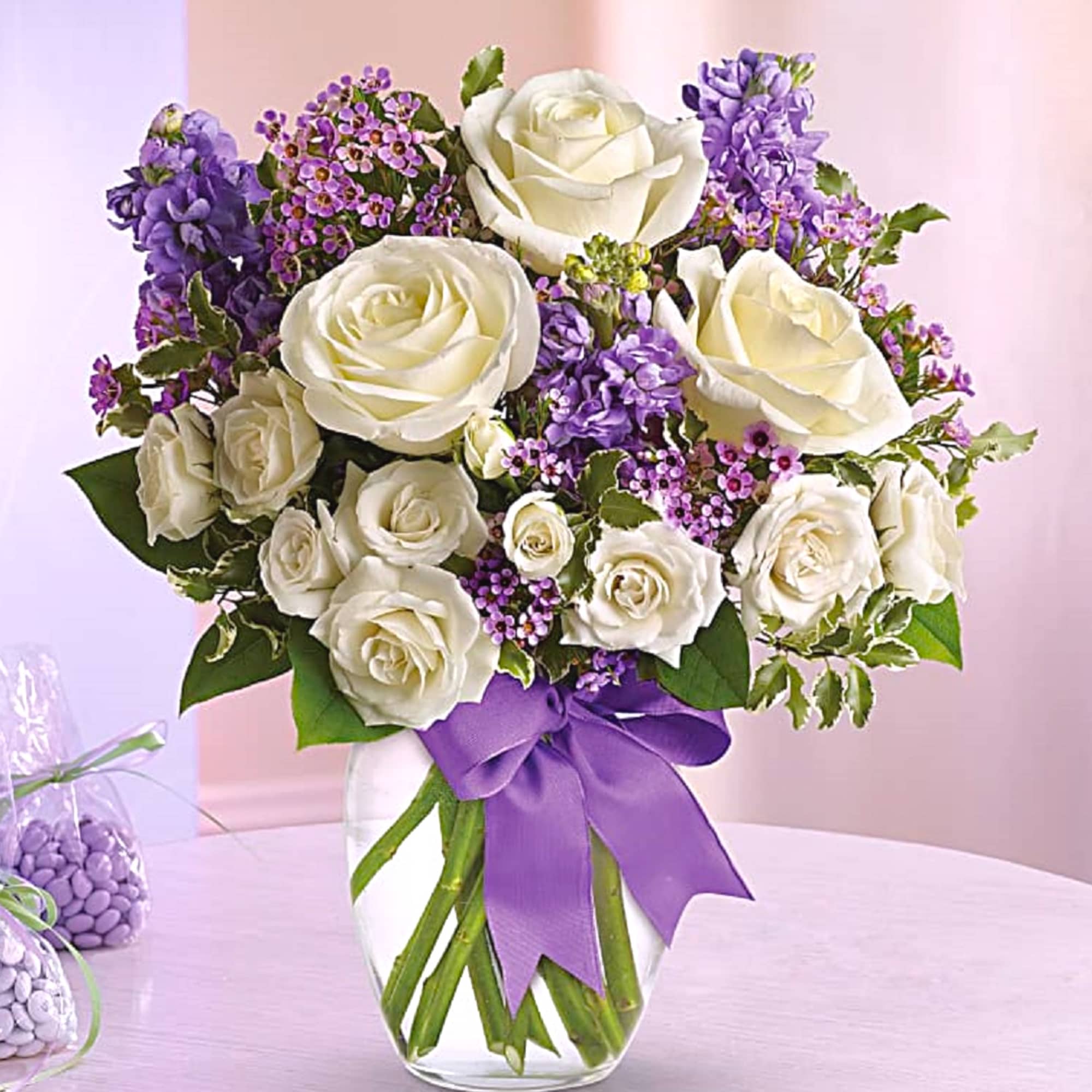 White roses and purple flowers in a glass vase with a purple ribbon