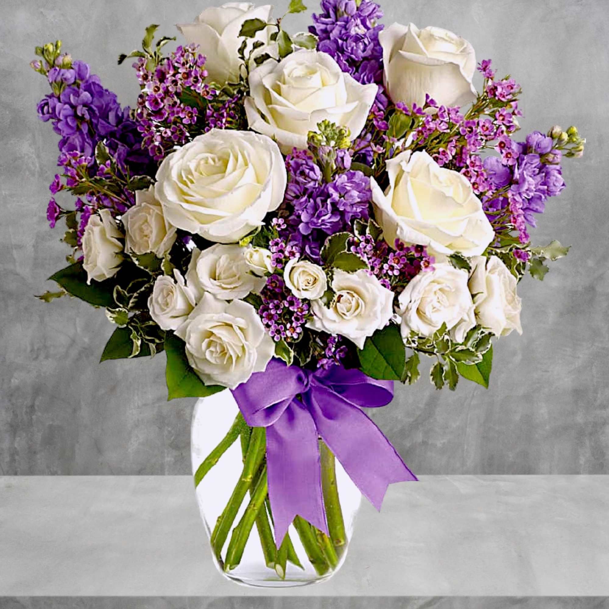 White roses and purple flowers arranged in a clear glass vase with a purple ribbon, photo 2 of 5