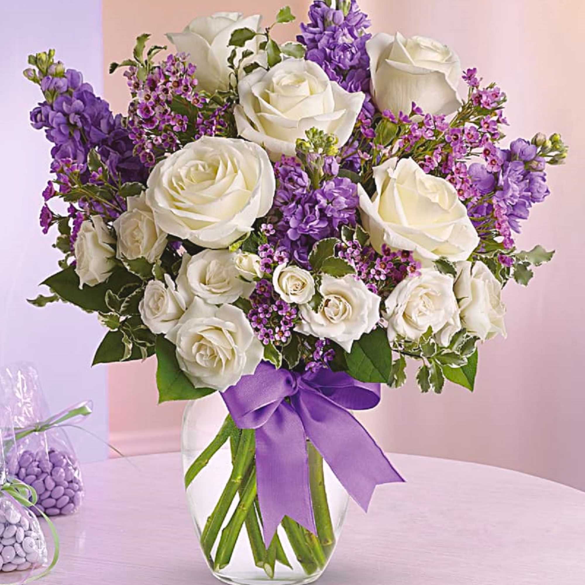 White roses and purple flowers in a clear glass vase with a purple ribbon, photo 3 of 5
