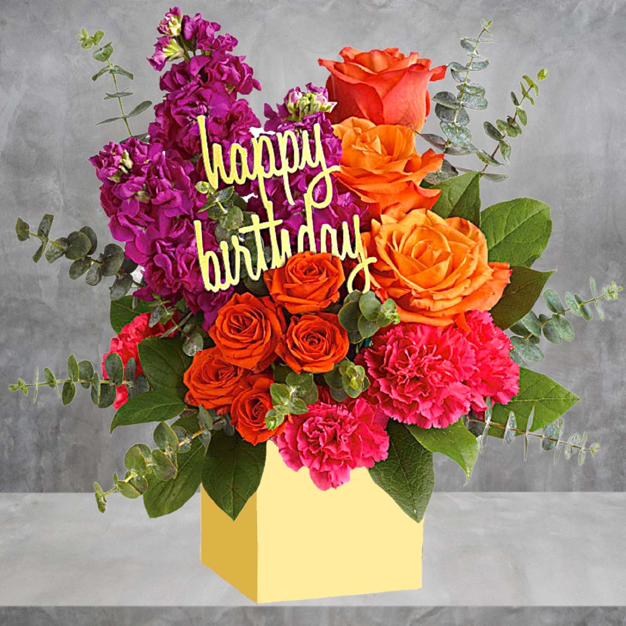 Birthday flower arrangement with roses, carnations, and a "happy birthday" sign in a yellow box