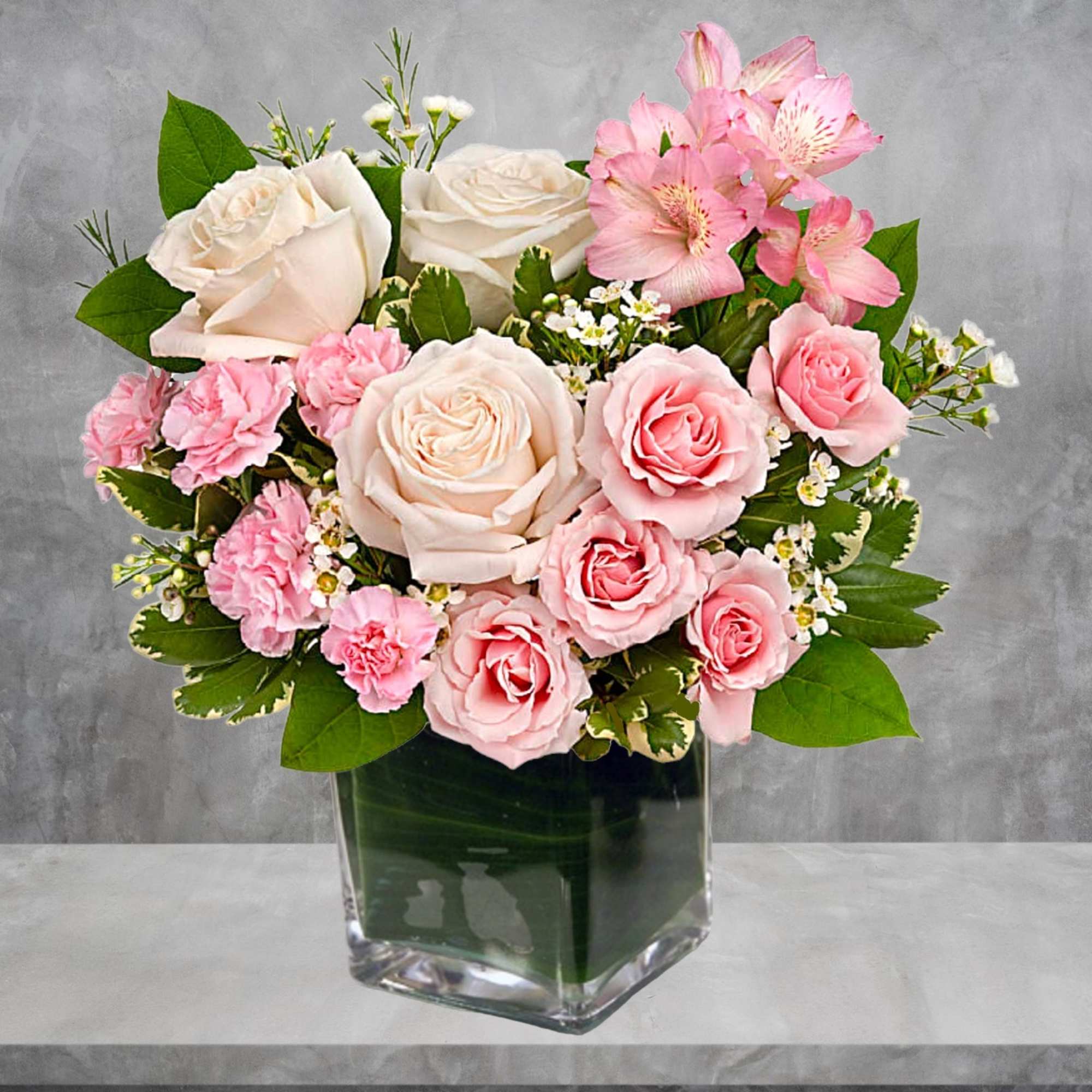 Pink and white roses with carnations in a clear square vase