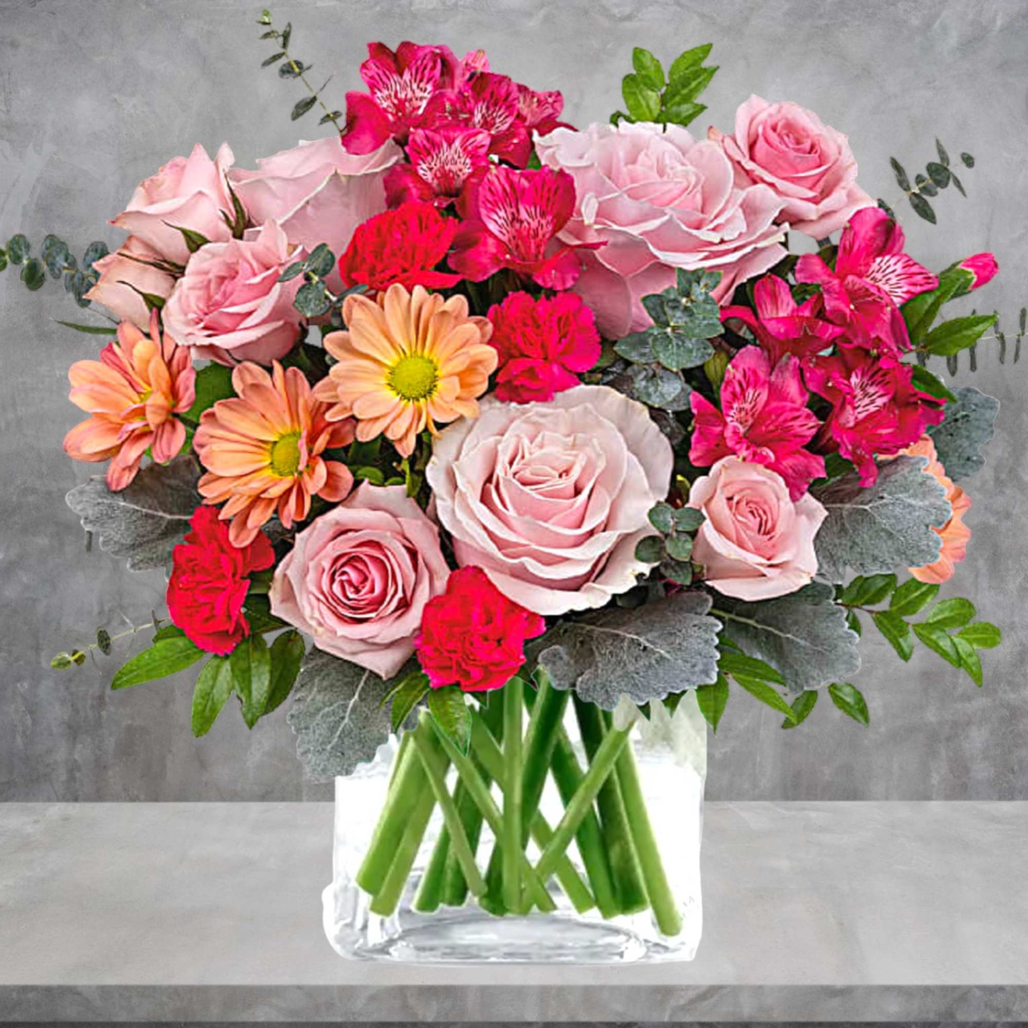 Pink roses and bright mixed flowers arranged in a clear glass vase.
