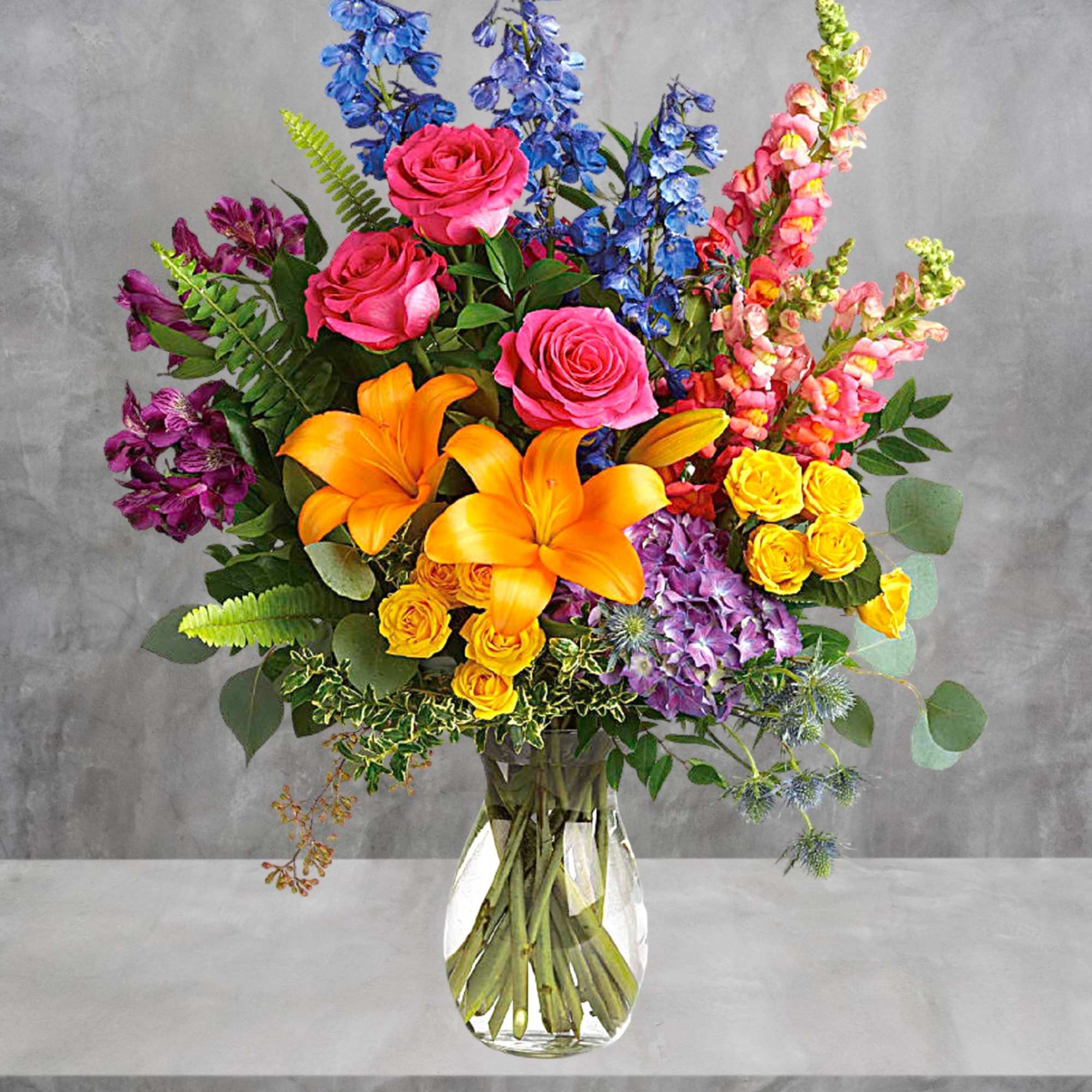 Colorful bouquet with roses, lilies, and snapdragons in a clear glass vase