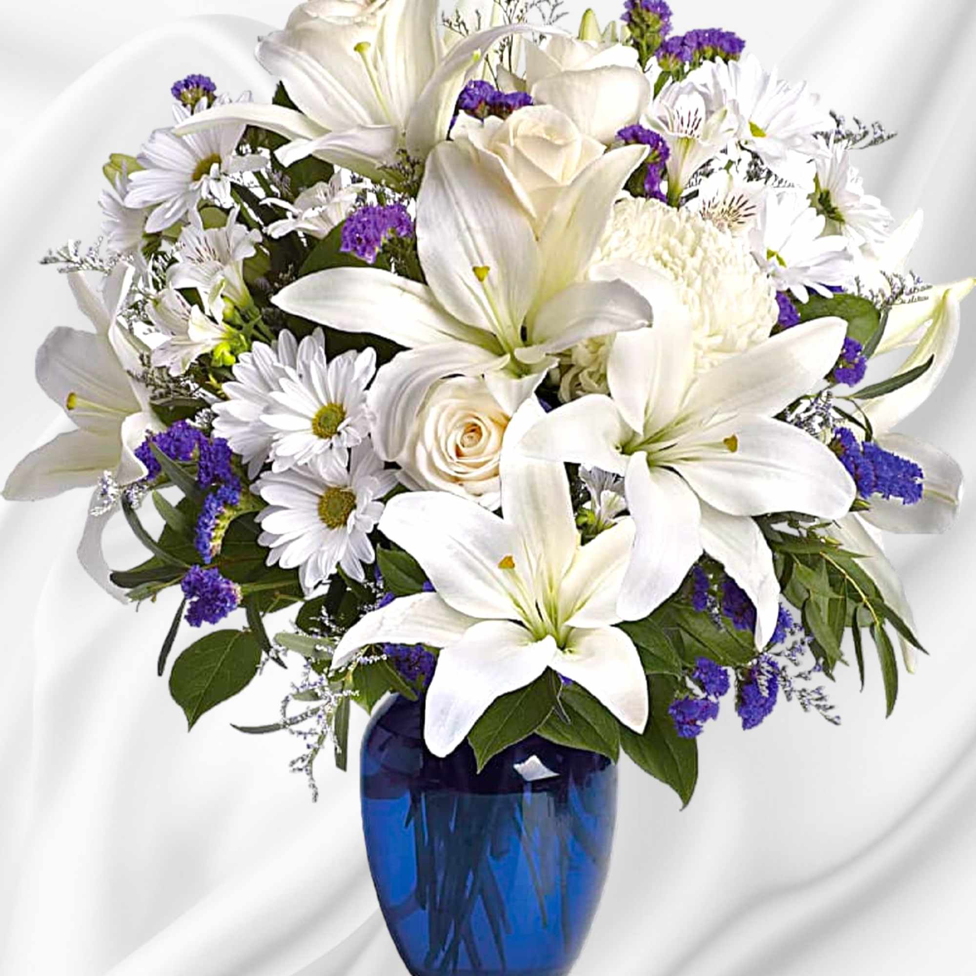 White lilies and daisies in a blue glass vase with purple accents