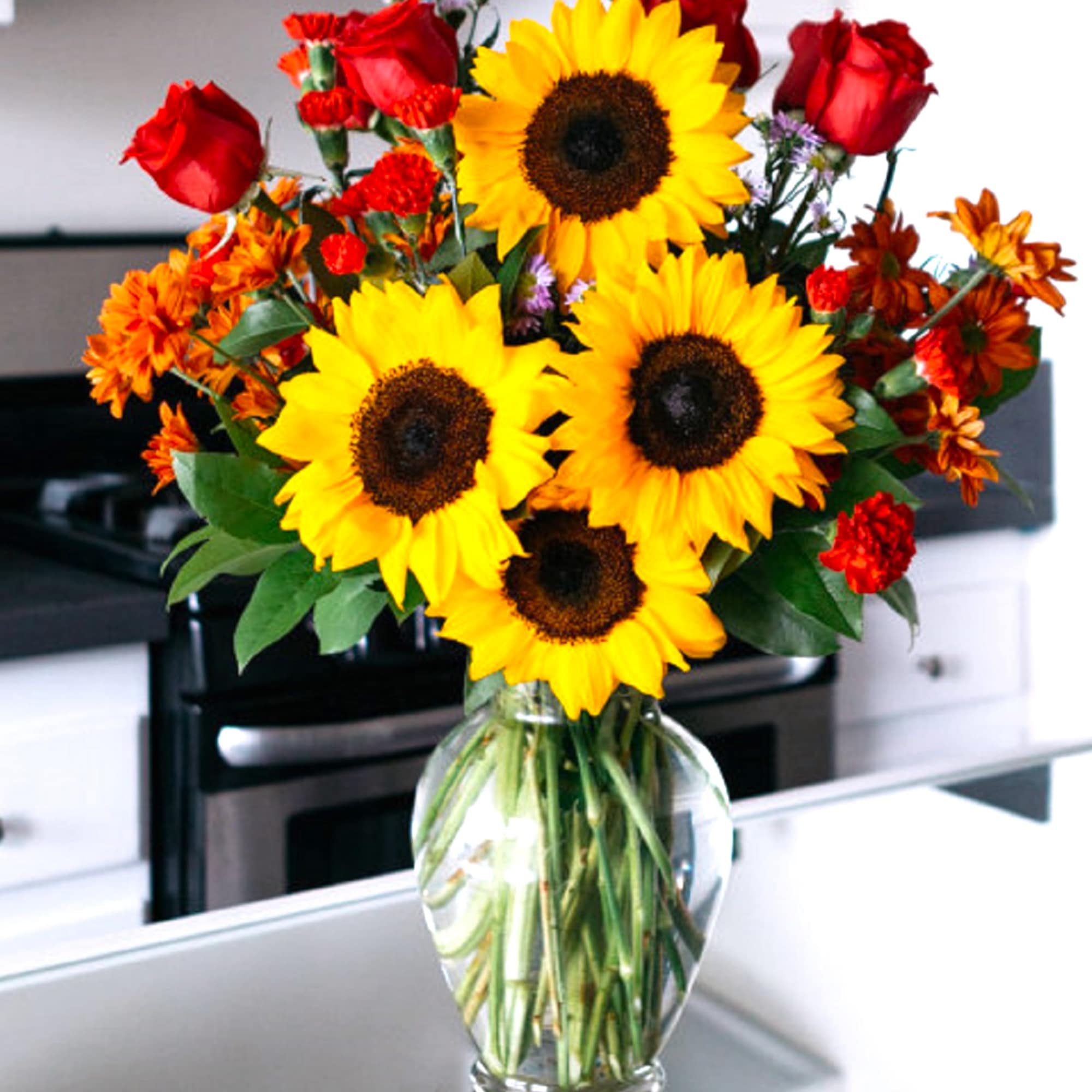 Bouquet of sunflowers, red roses, and orange flowers in a glass vase