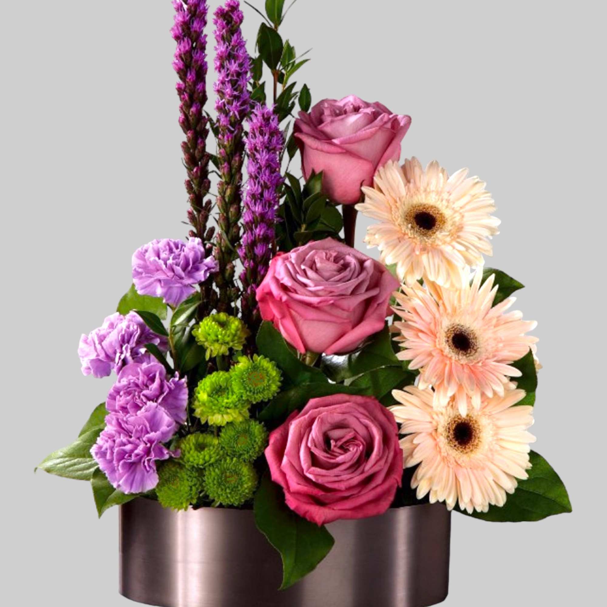 Pink roses, gerbera daisies, and purple flowers in a round box
