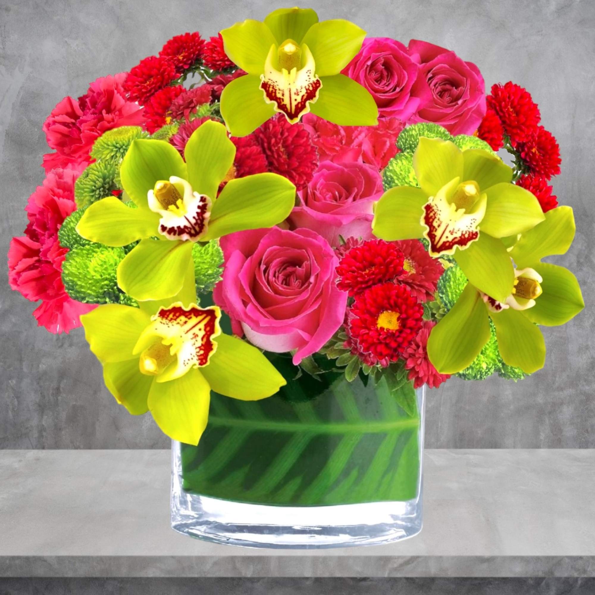 Bouquet of pink roses, red flowers, and lime green orchids in a glass vase