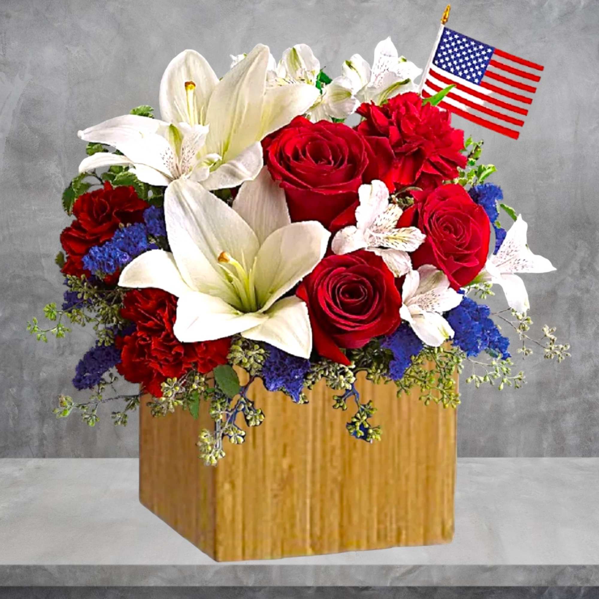 Red roses and white lilies arranged in a wooden box with a small American flag.