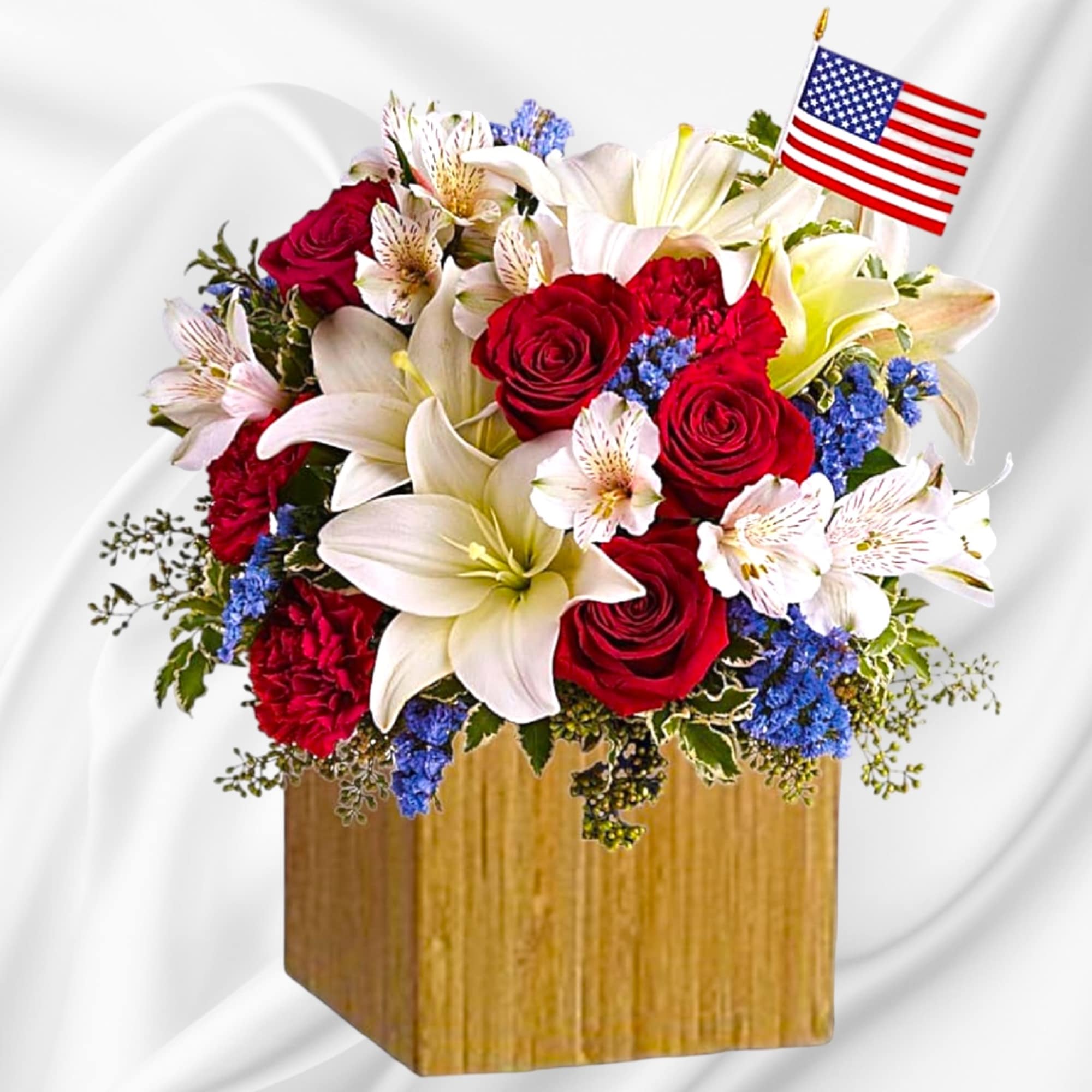 Red roses and white lilies in a wooden cube vase with a small American flag
