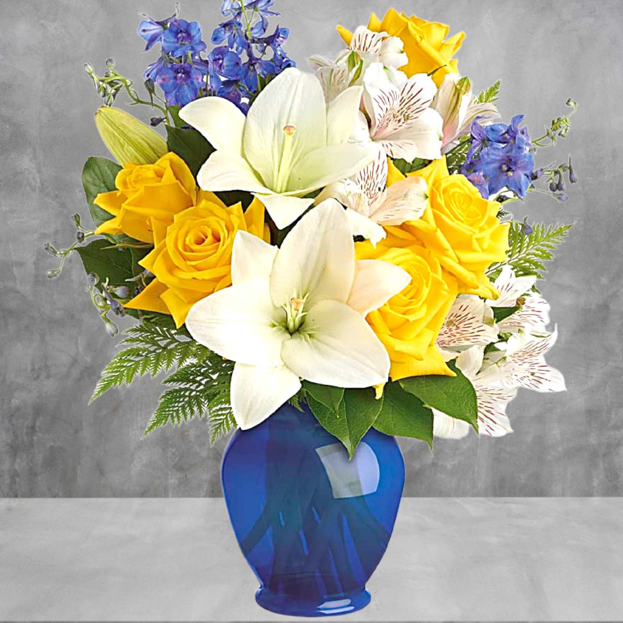 Bouquet of yellow roses, white lilies, and blue flowers in a blue vase