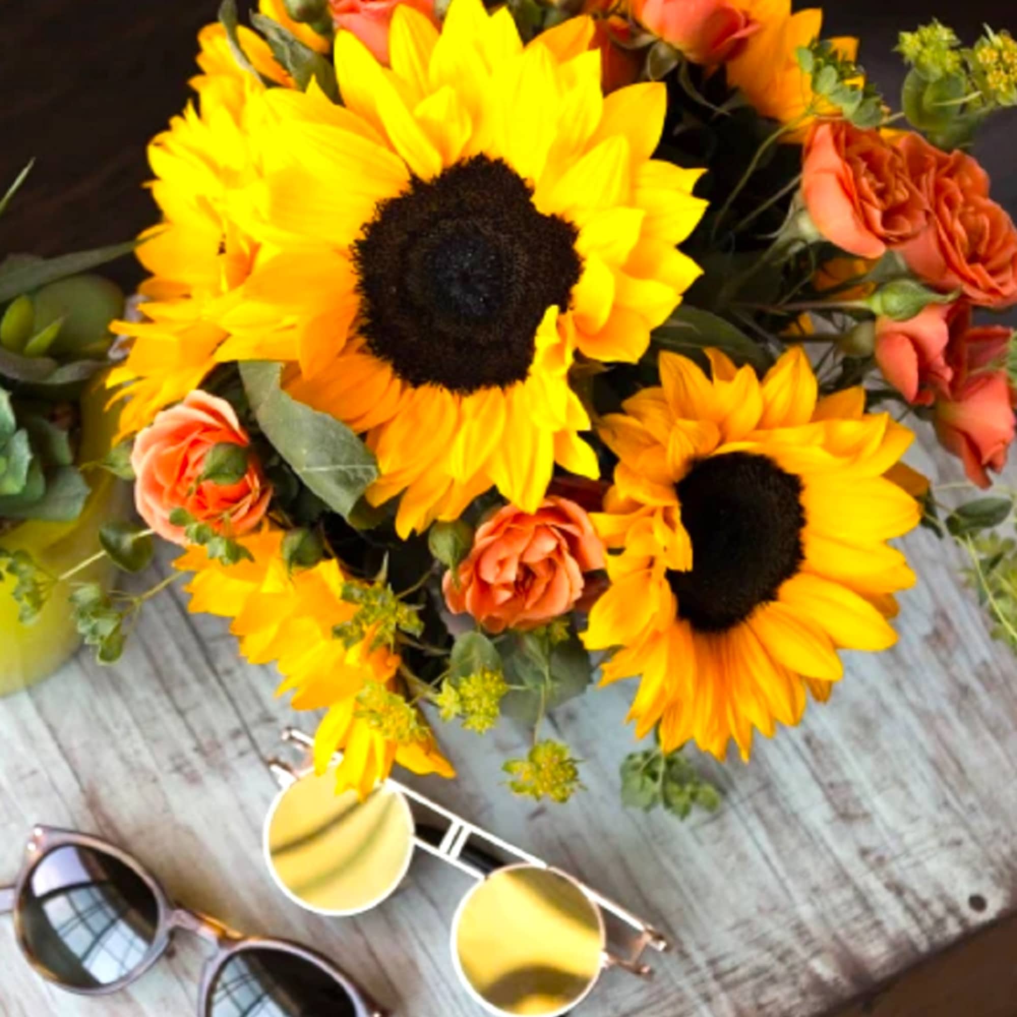 Bouquet of sunflowers and peach roses on a table with sunglasses