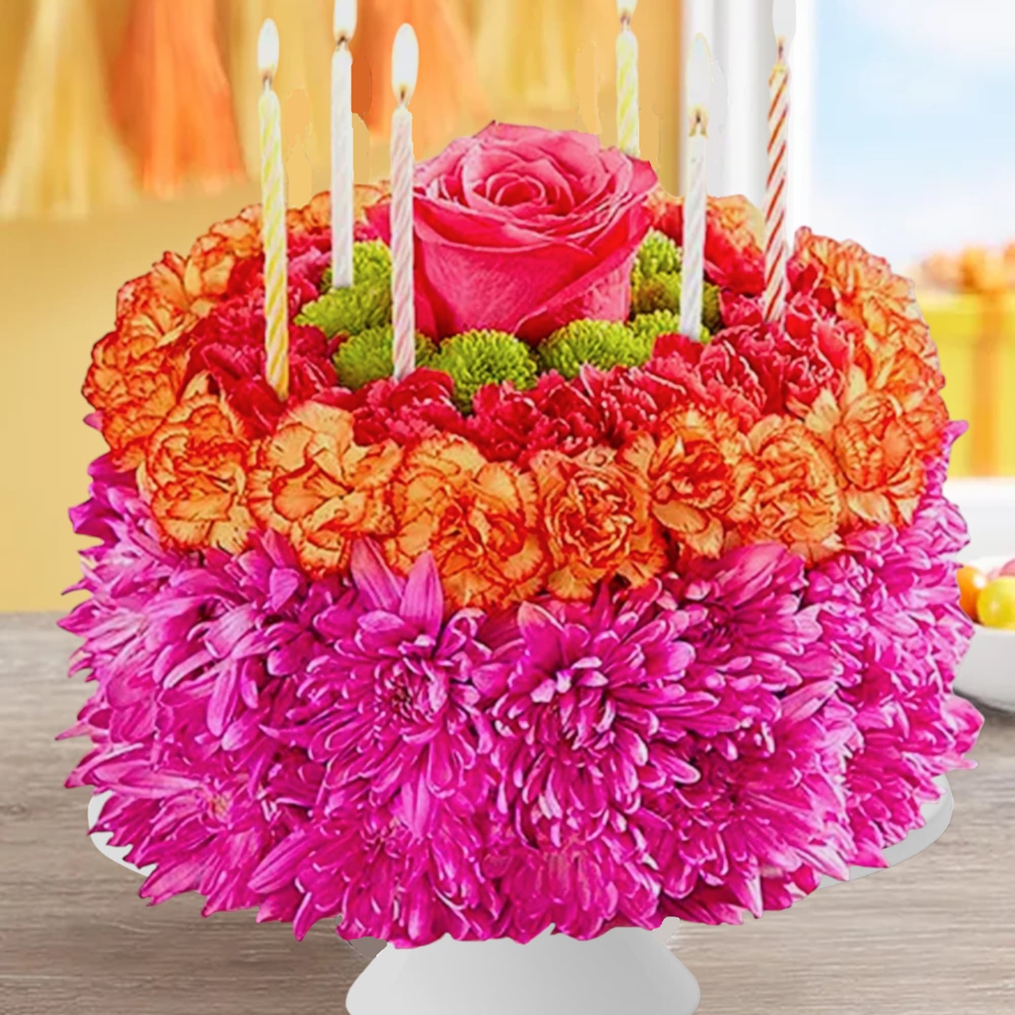 Bright floral birthday cake with candles on a white stand