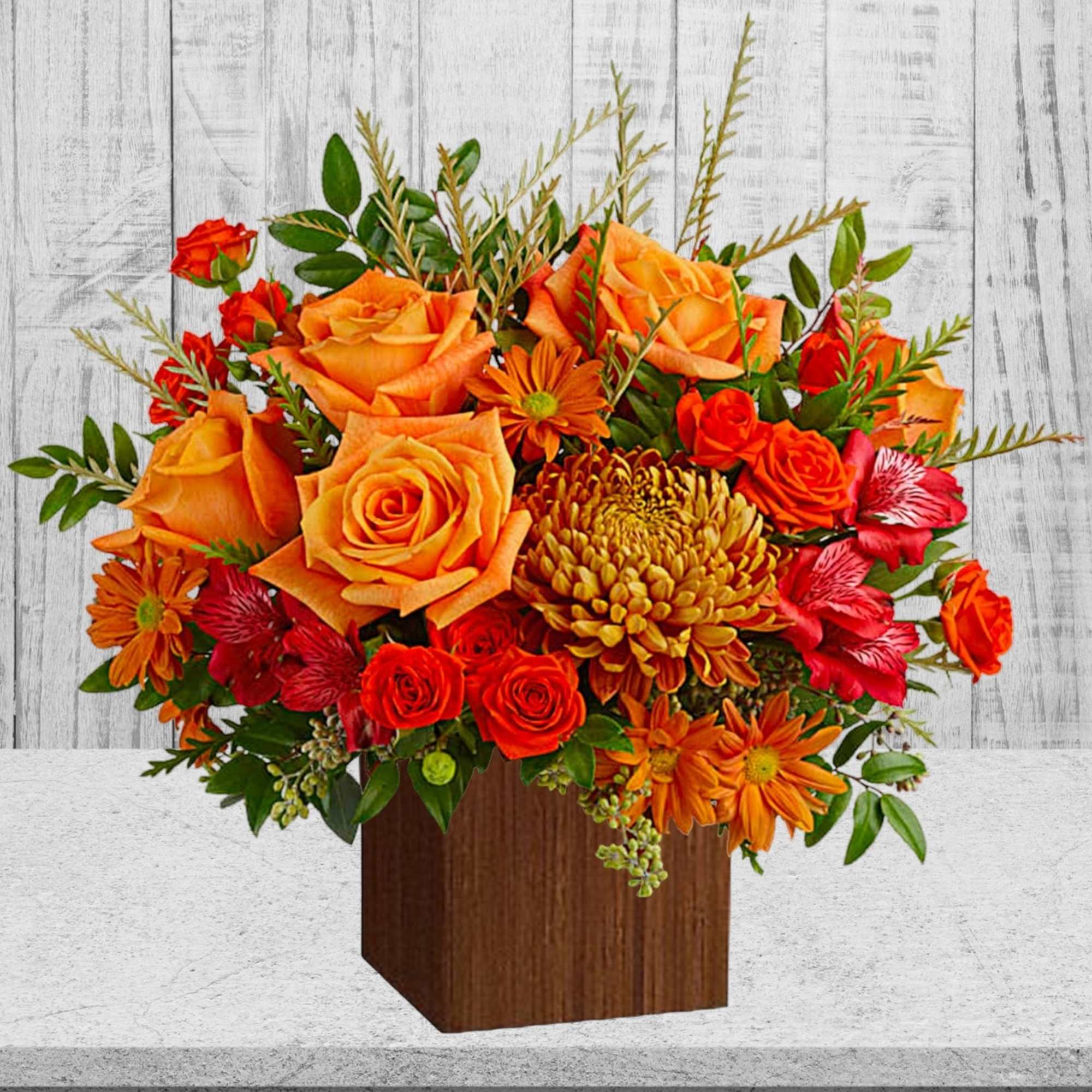 Orange and red flower arrangement in a wooden cube vase