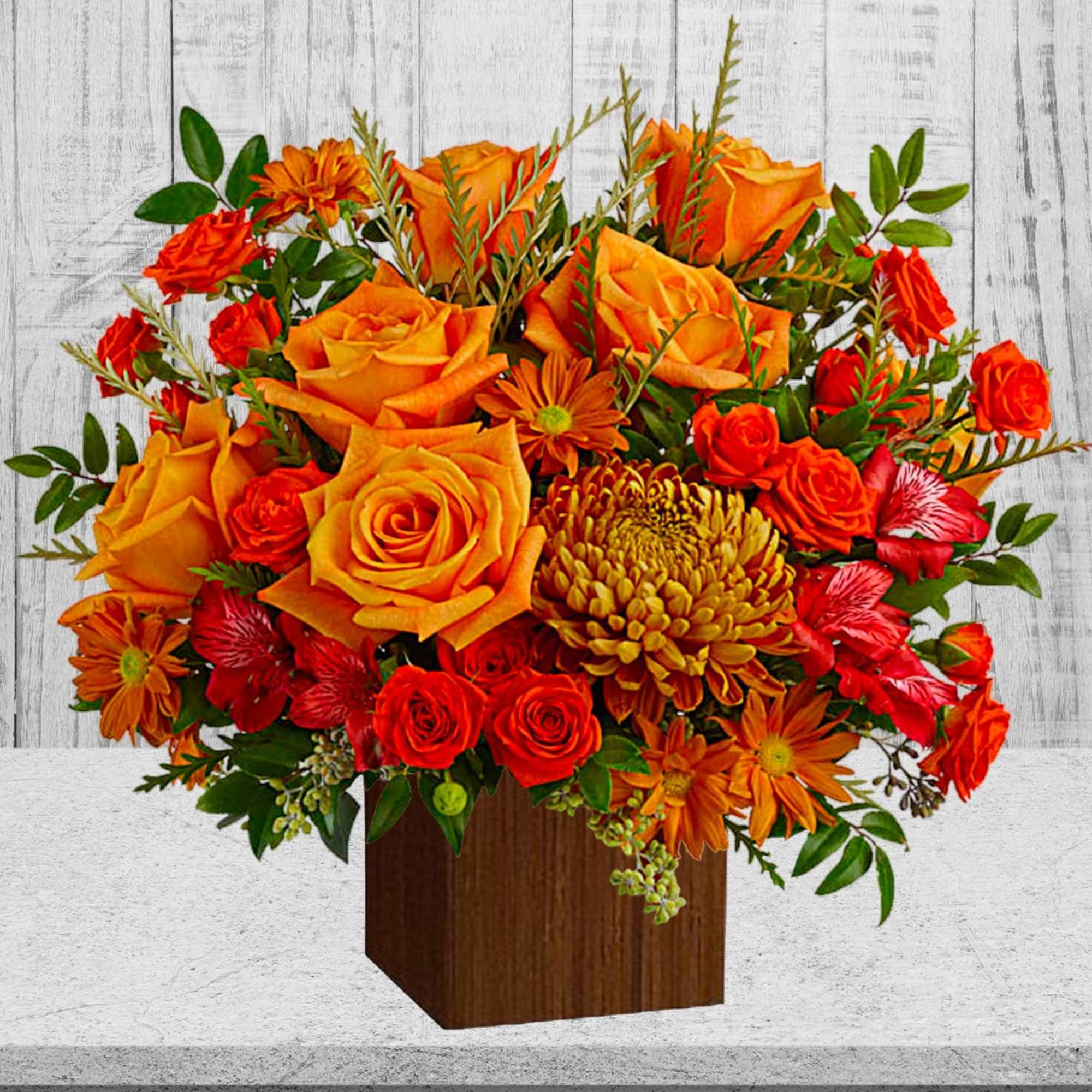 Orange and red flower arrangement in a wooden cube vase