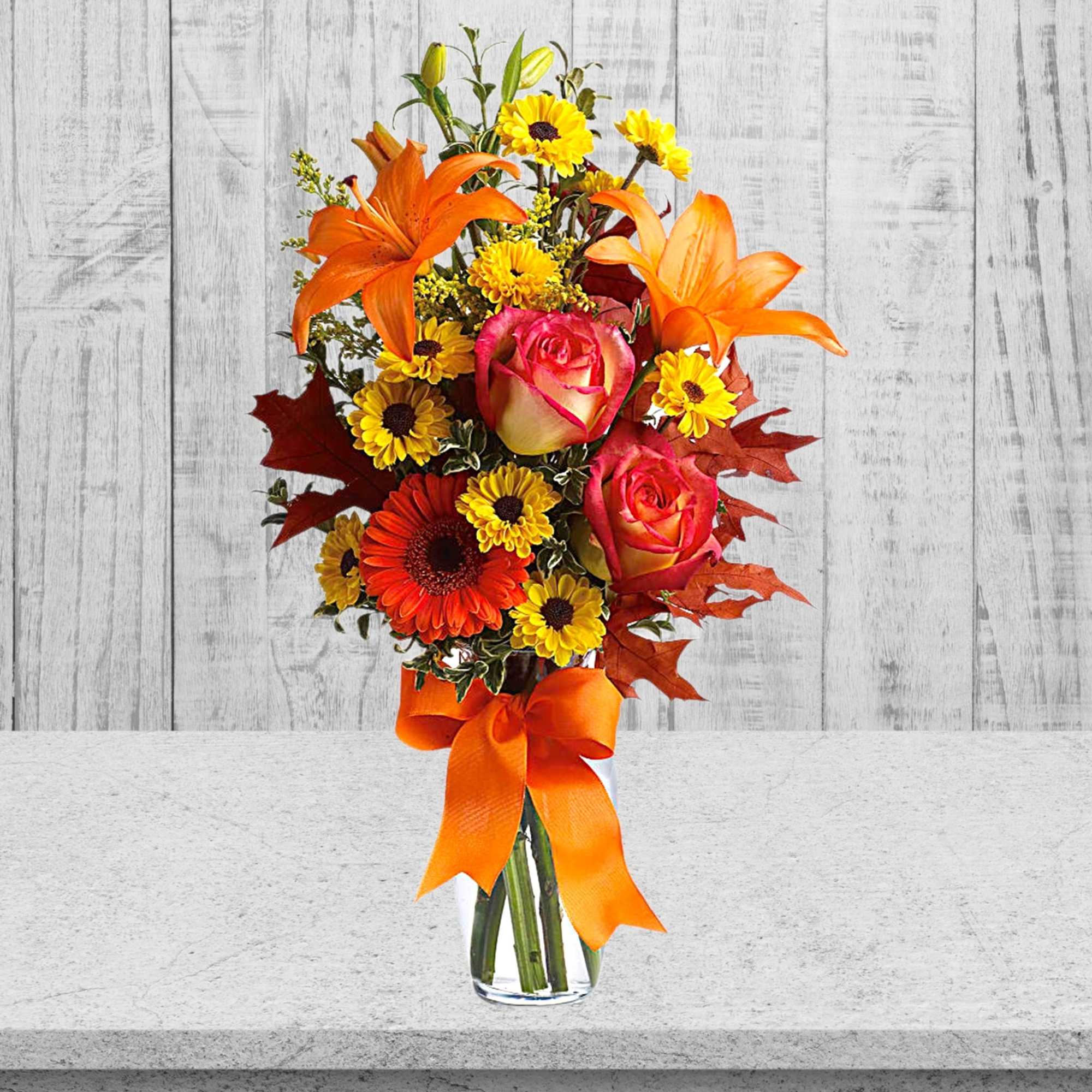 Orange lilies and pink roses in a clear glass vase with an orange ribbon