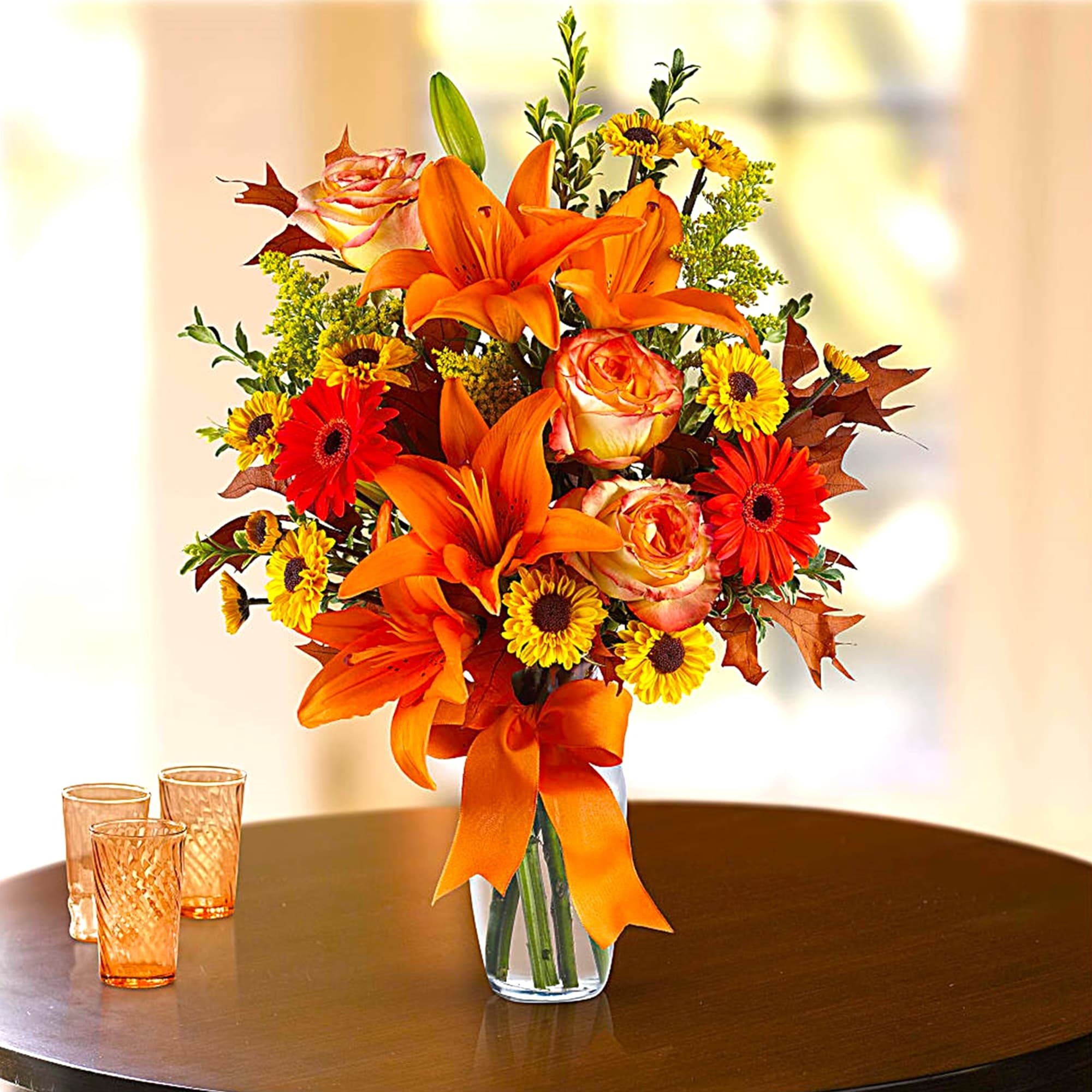 Orange lilies and roses in a clear glass vase with a ribbon