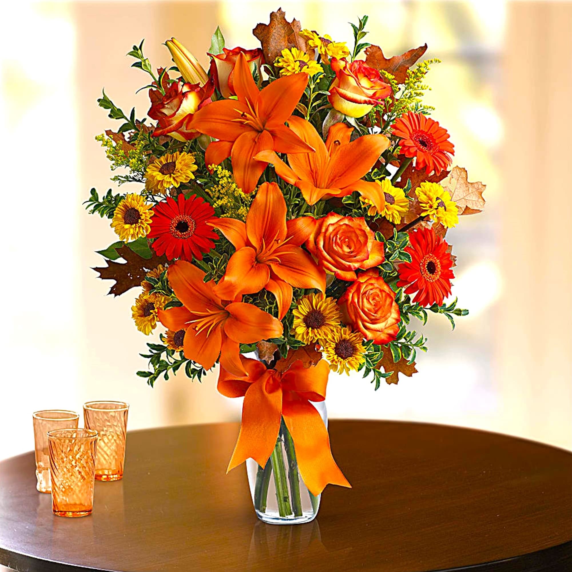 Orange lilies and roses in a glass vase with a ribbon