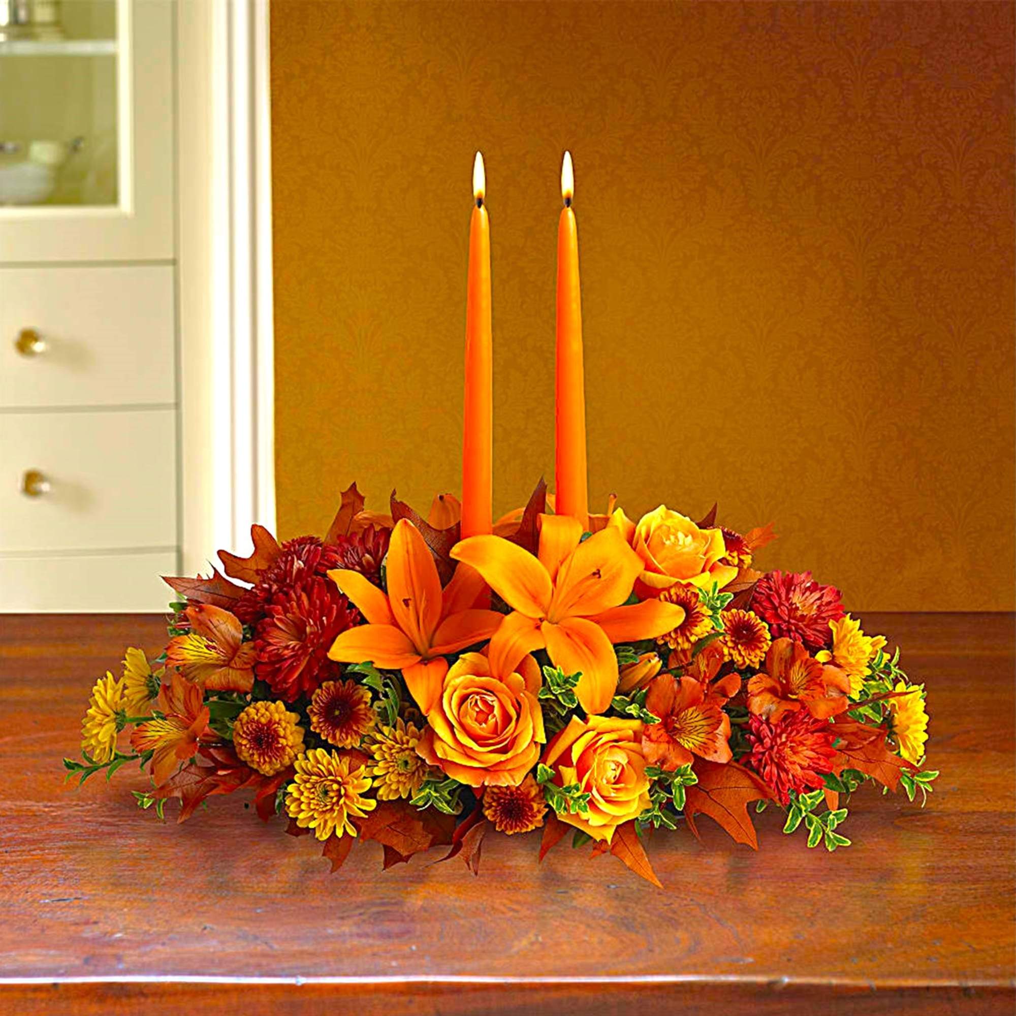 Orange floral centerpiece with two tall taper candles