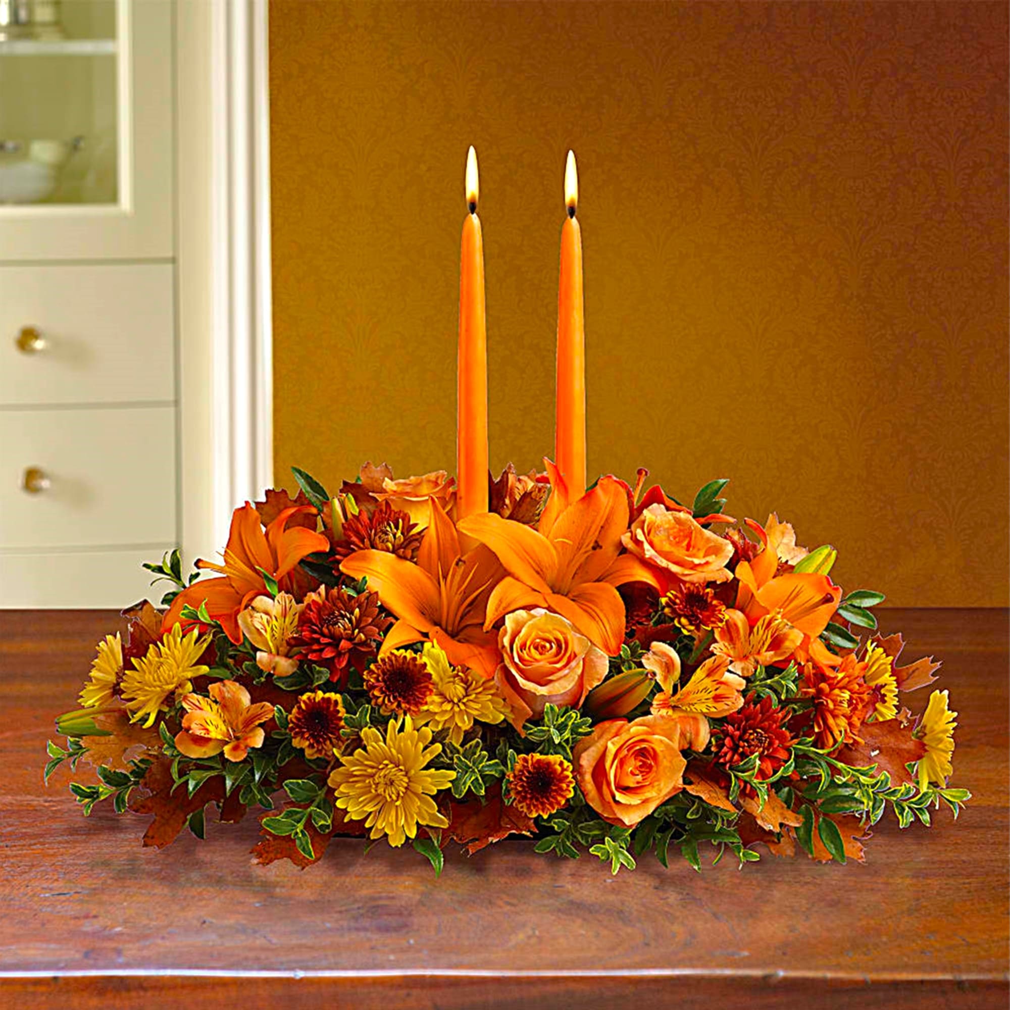 Orange floral centerpiece with two tall taper candles