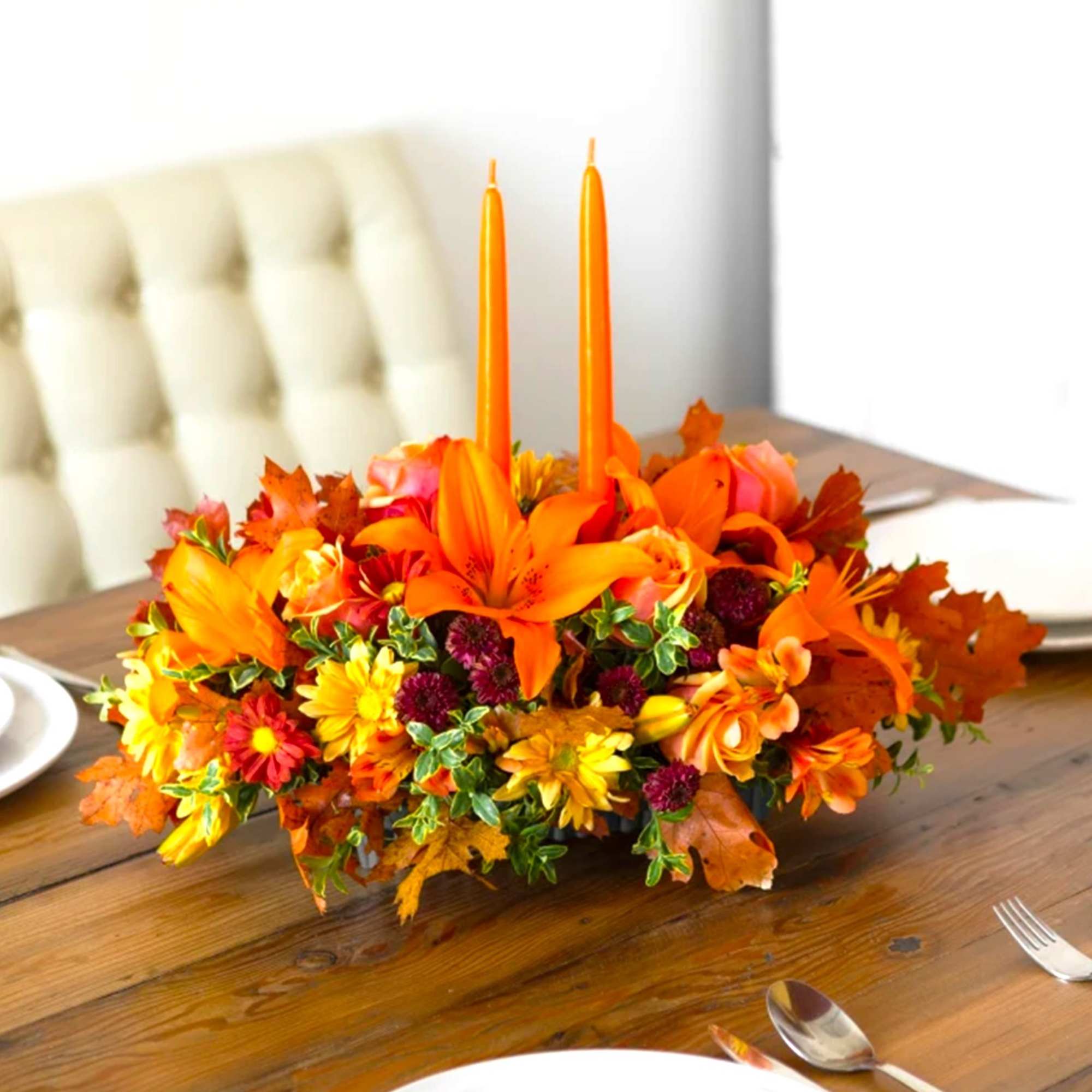Orange floral centerpiece with two tall candles on a dining table