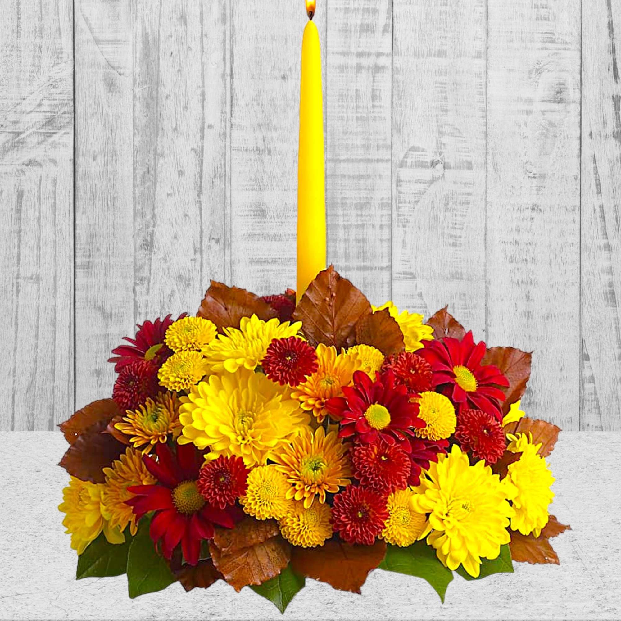 Yellow taper candle in a low arrangement of red and yellow chrysanthemums, photo 2 of 4