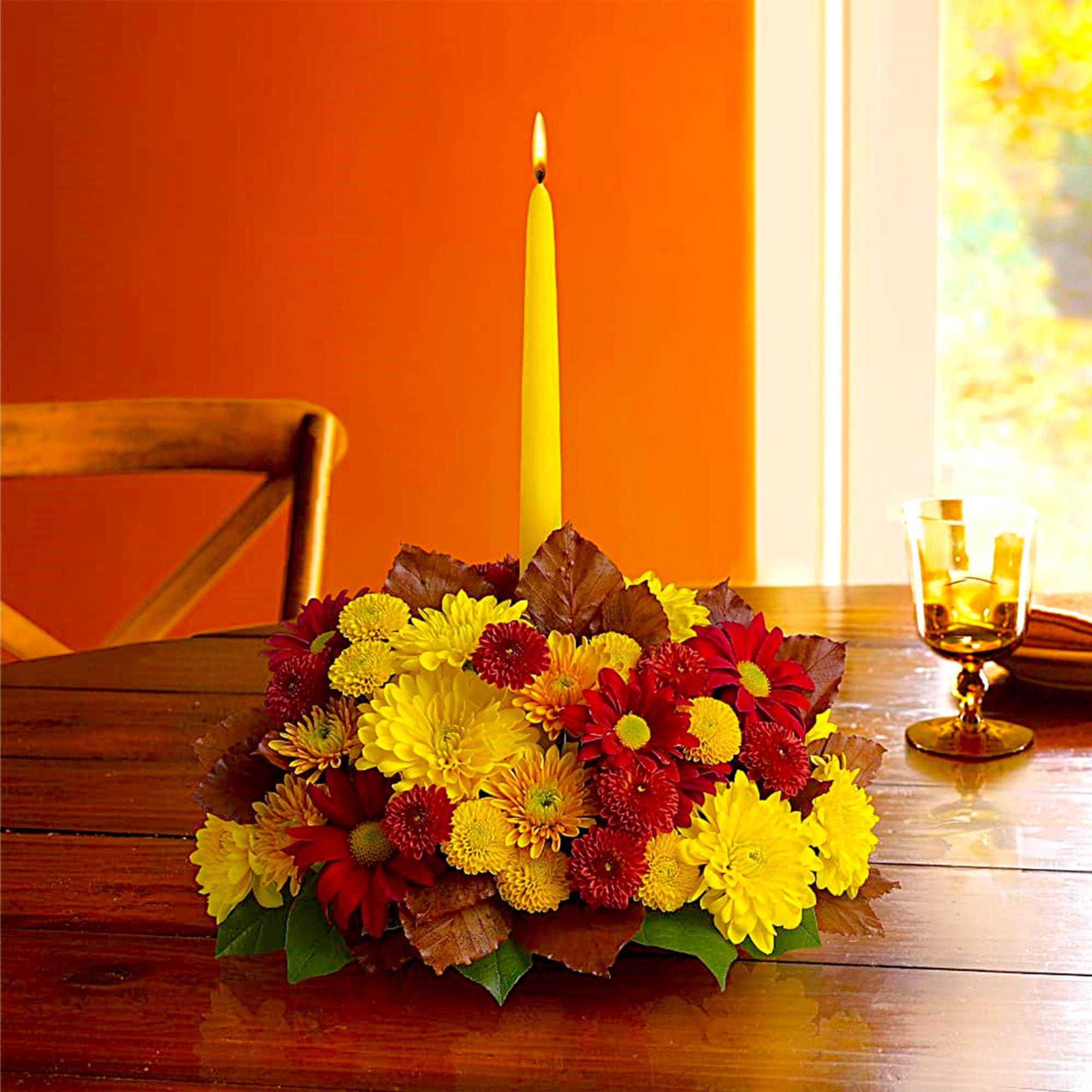 Low centerpiece of yellow and red chrysanthemums with a tall candle