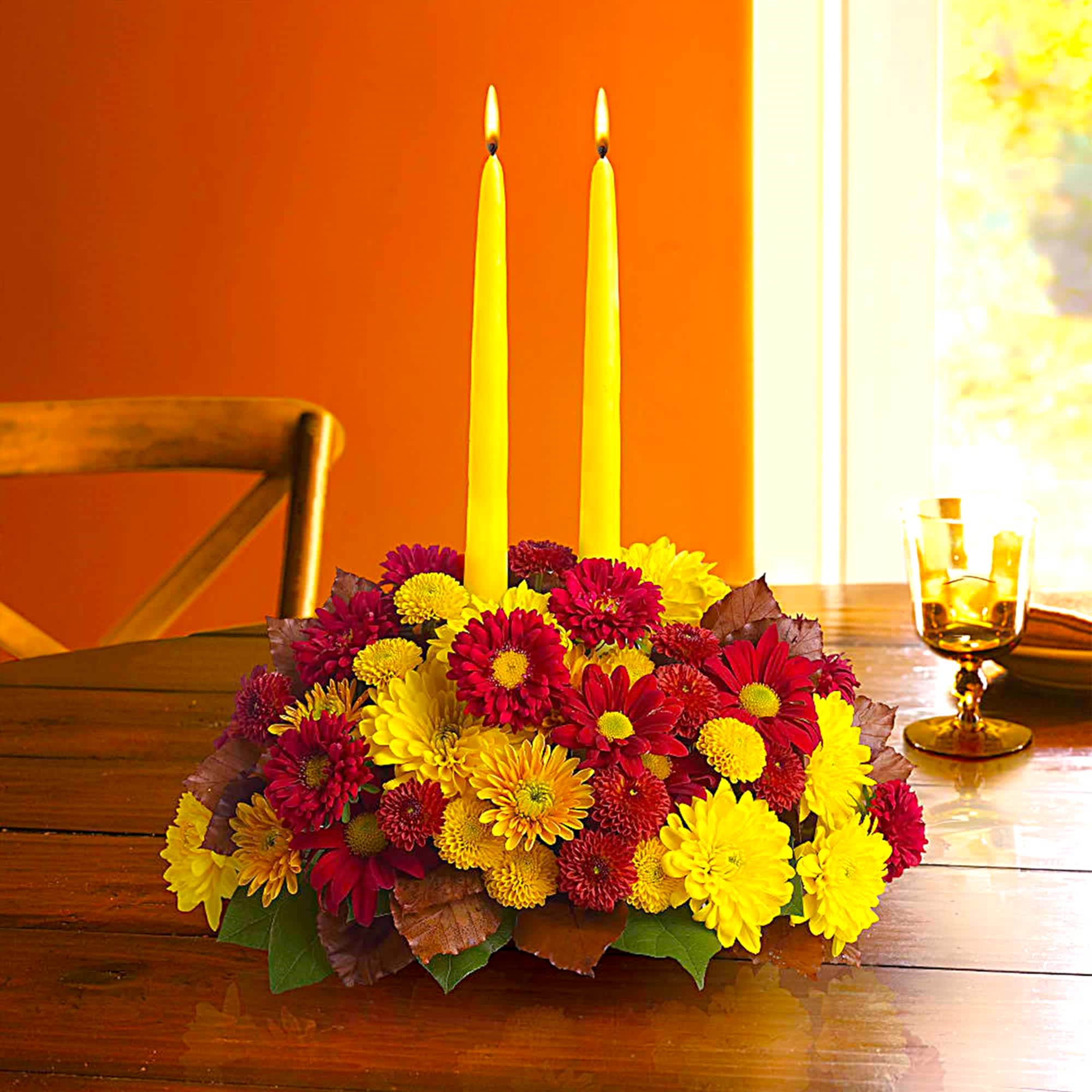 Low floral centerpiece with yellow candles and red and yellow mums