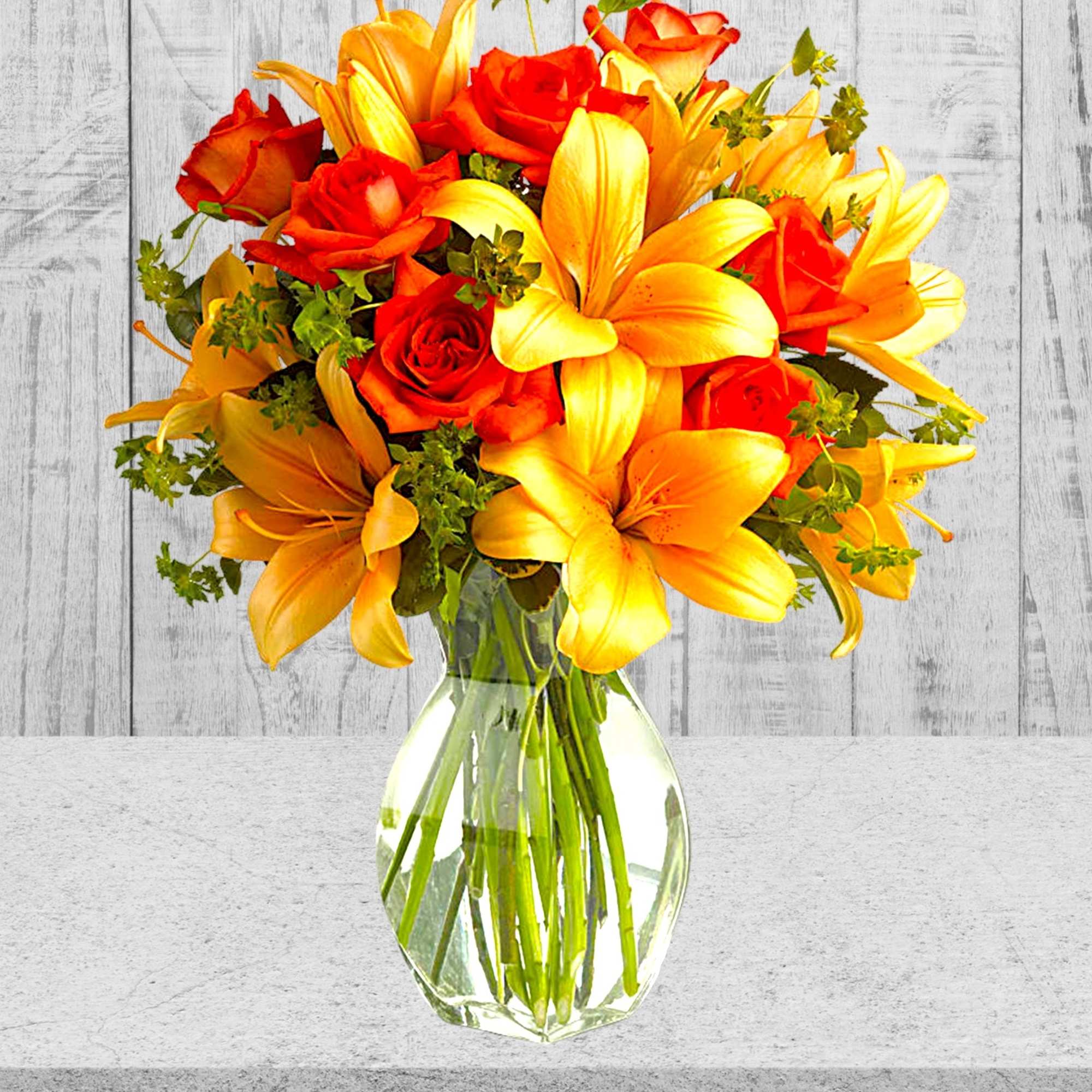 Bouquet of orange and yellow lilies and red roses in a clear glass vase