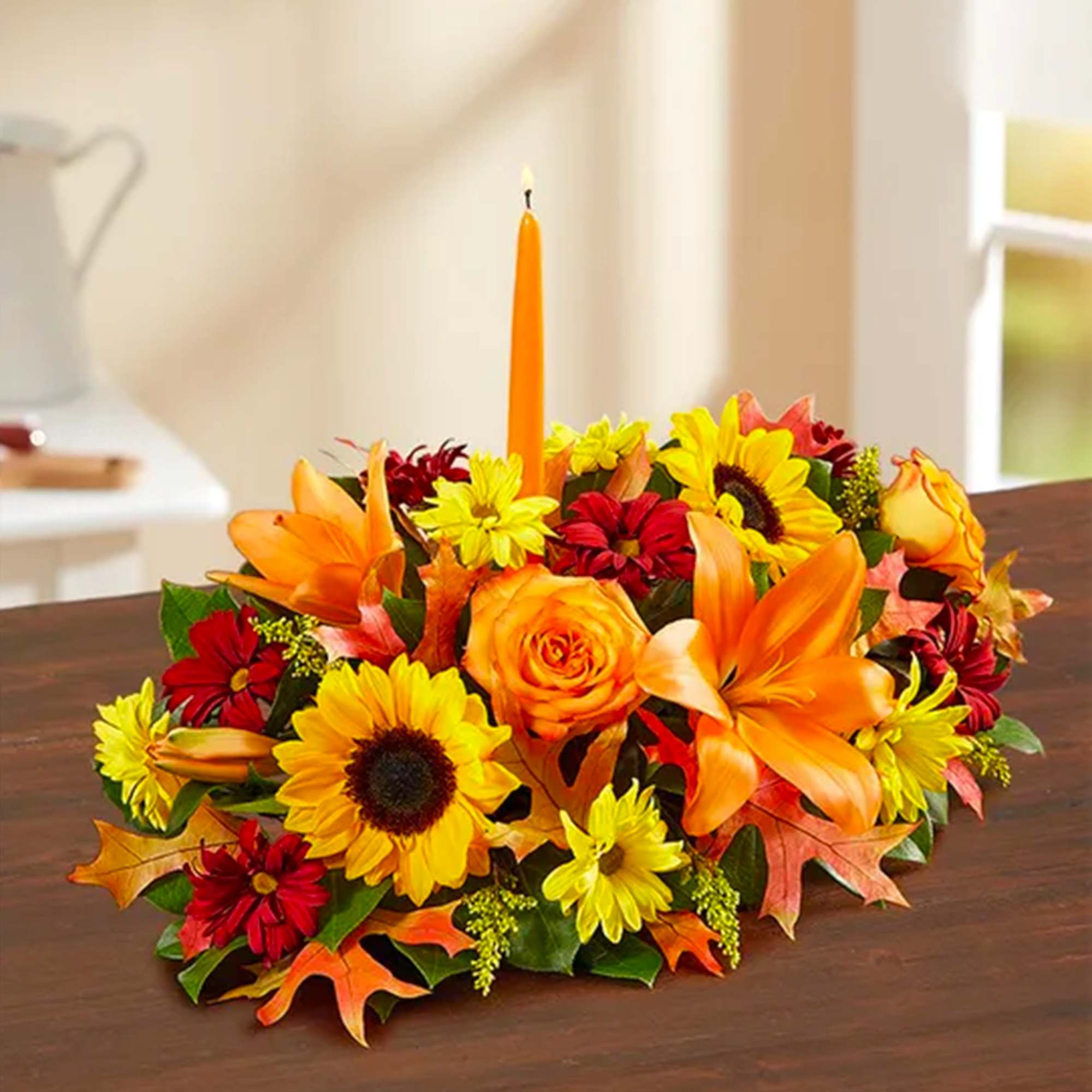 Autumn floral centerpiece with orange lilies, sunflowers, and a tall candle