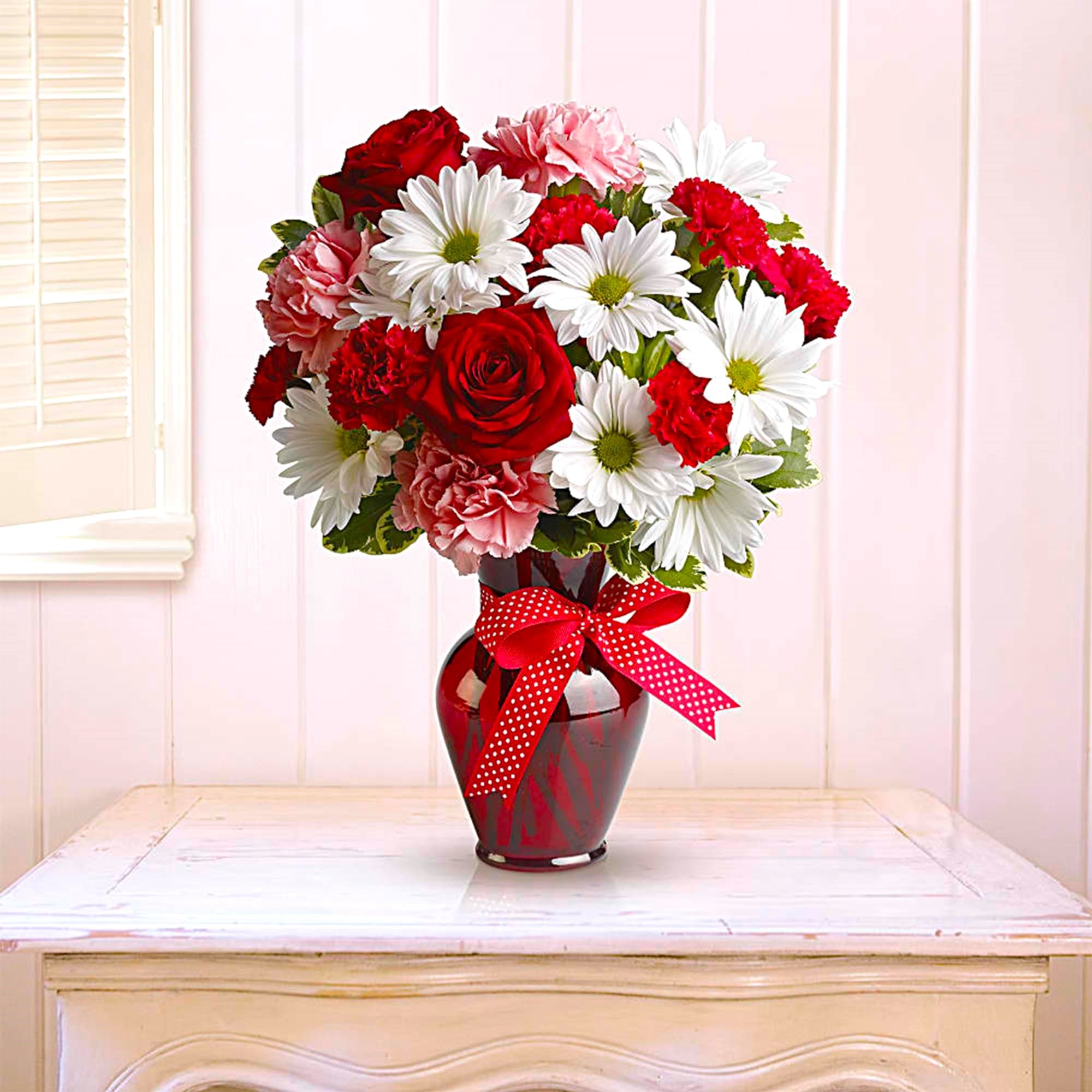 Bouquet of red roses, pink carnations, and white daisies in a red vase