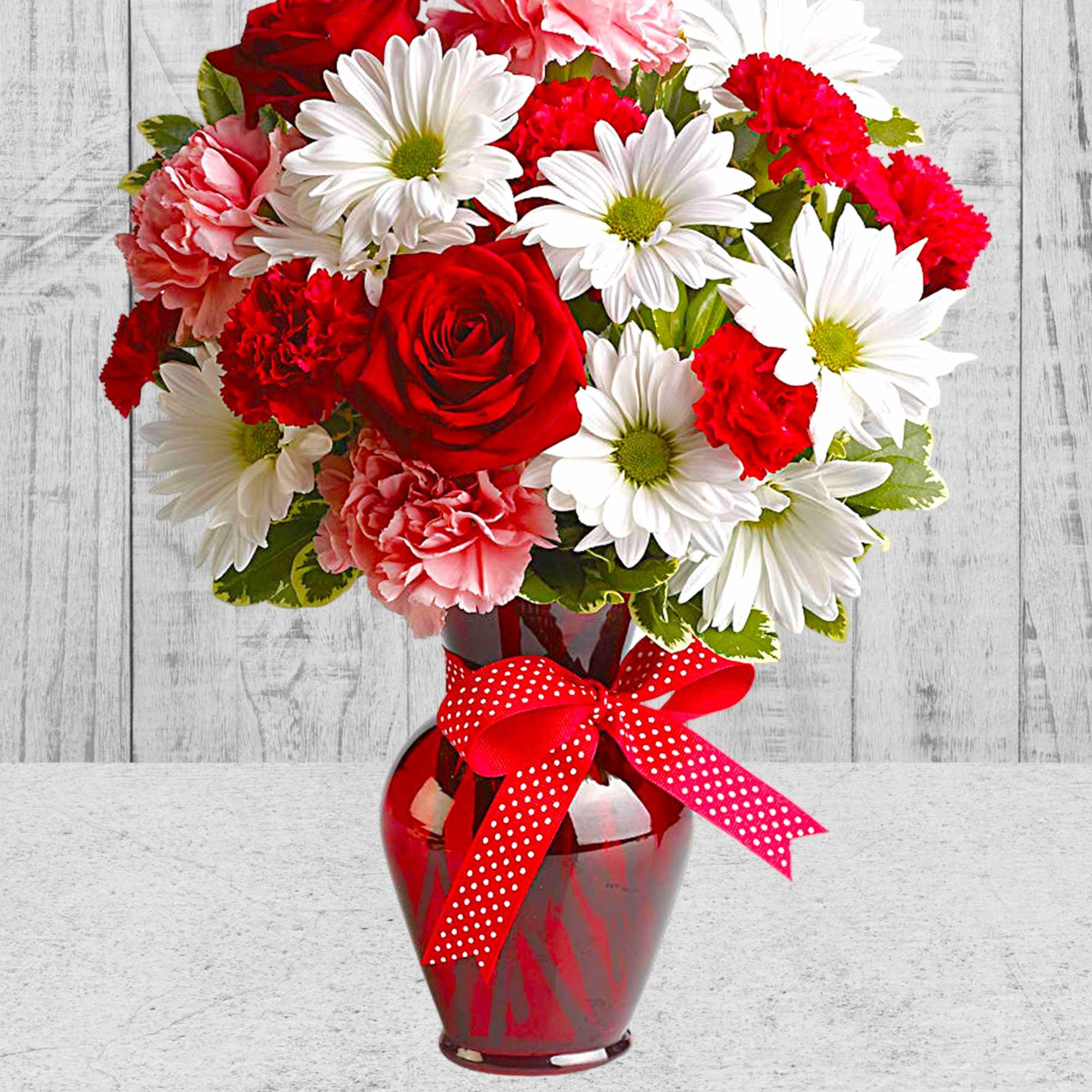 Bouquet of red roses, white daisies, and pink carnations in a red vase with a ribbon, photo 3 of 5