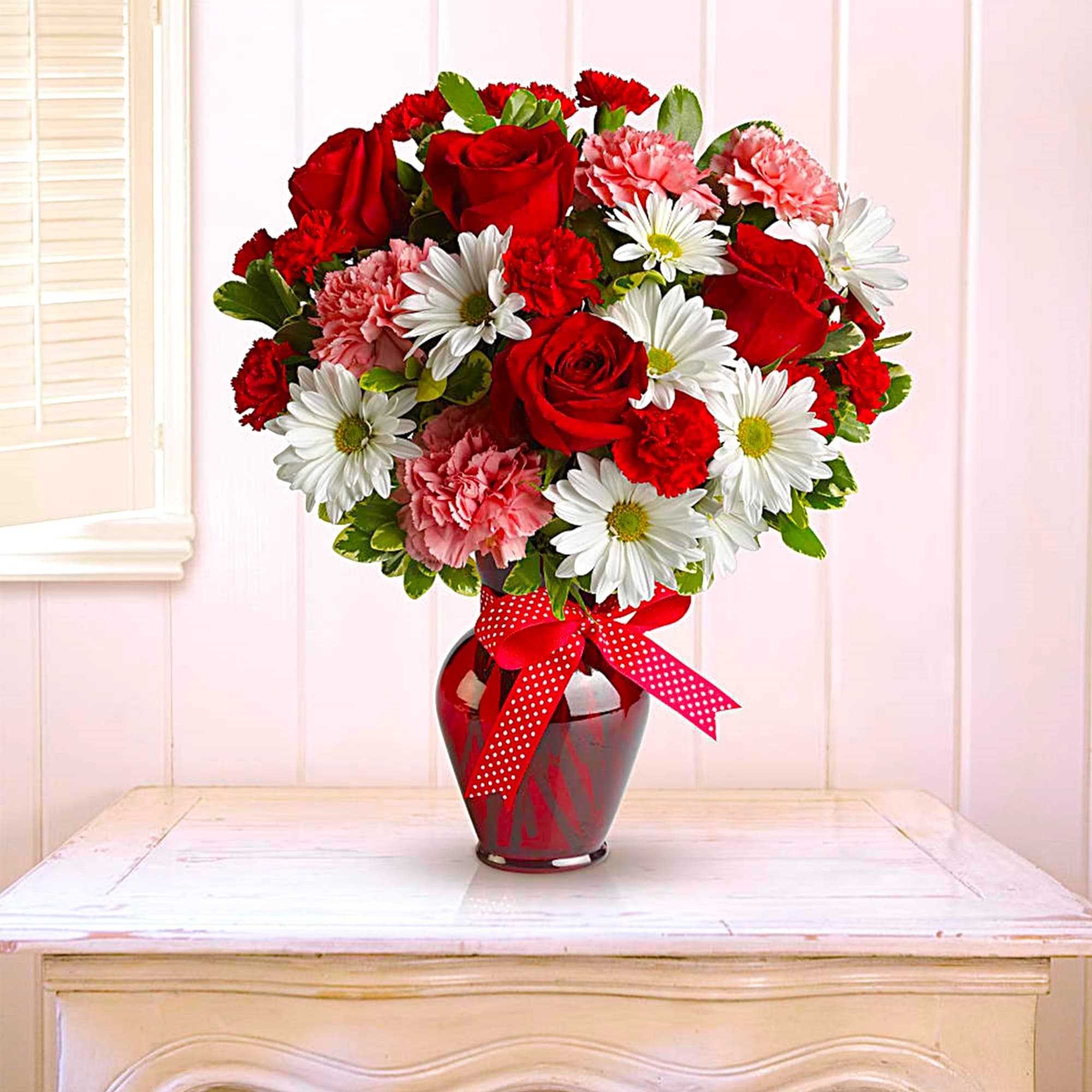 Bouquet of red roses, white daisies, and pink carnations in a red vase