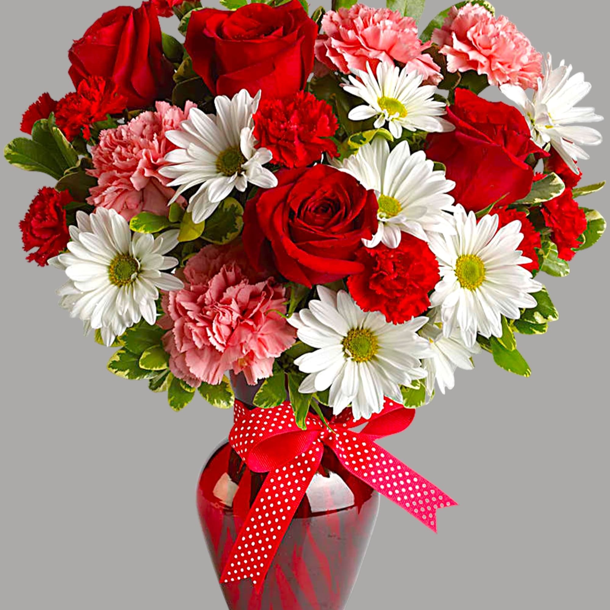 Red roses, pink carnations, and white daisies in a red glass vase with a ribbon
