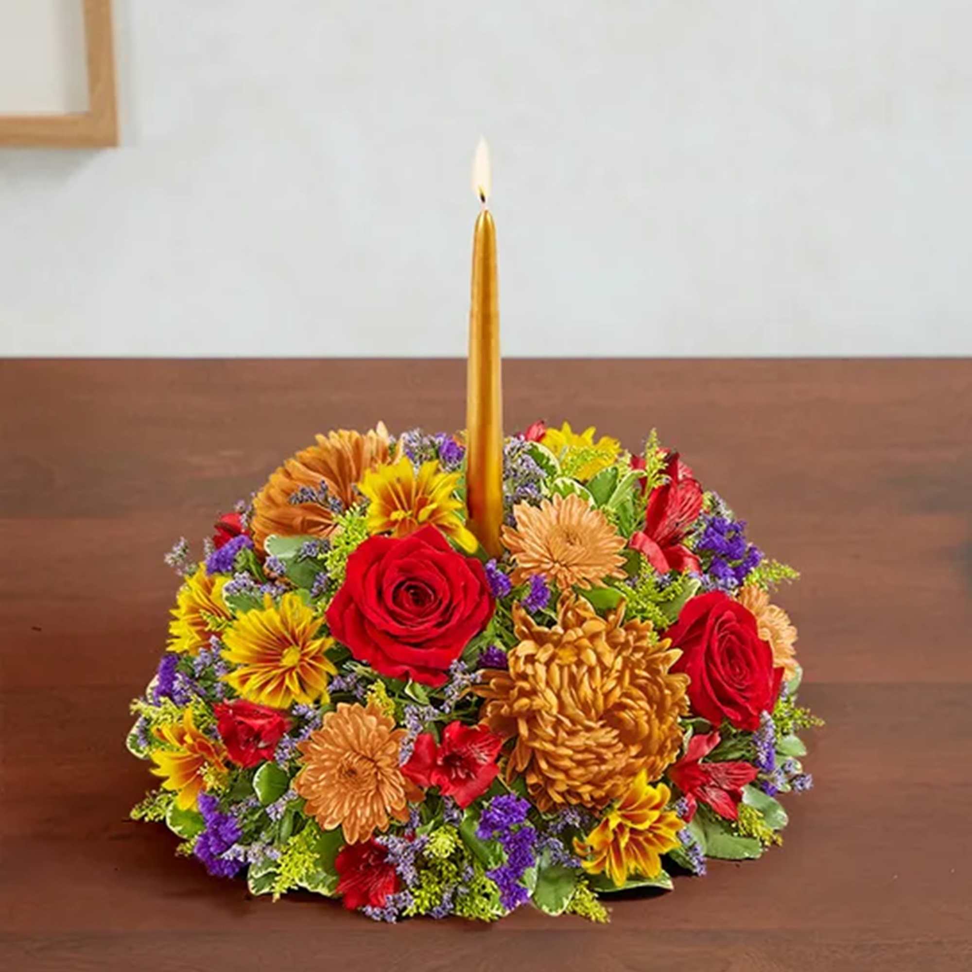 Colorful floral centerpiece with a lit gold taper candle