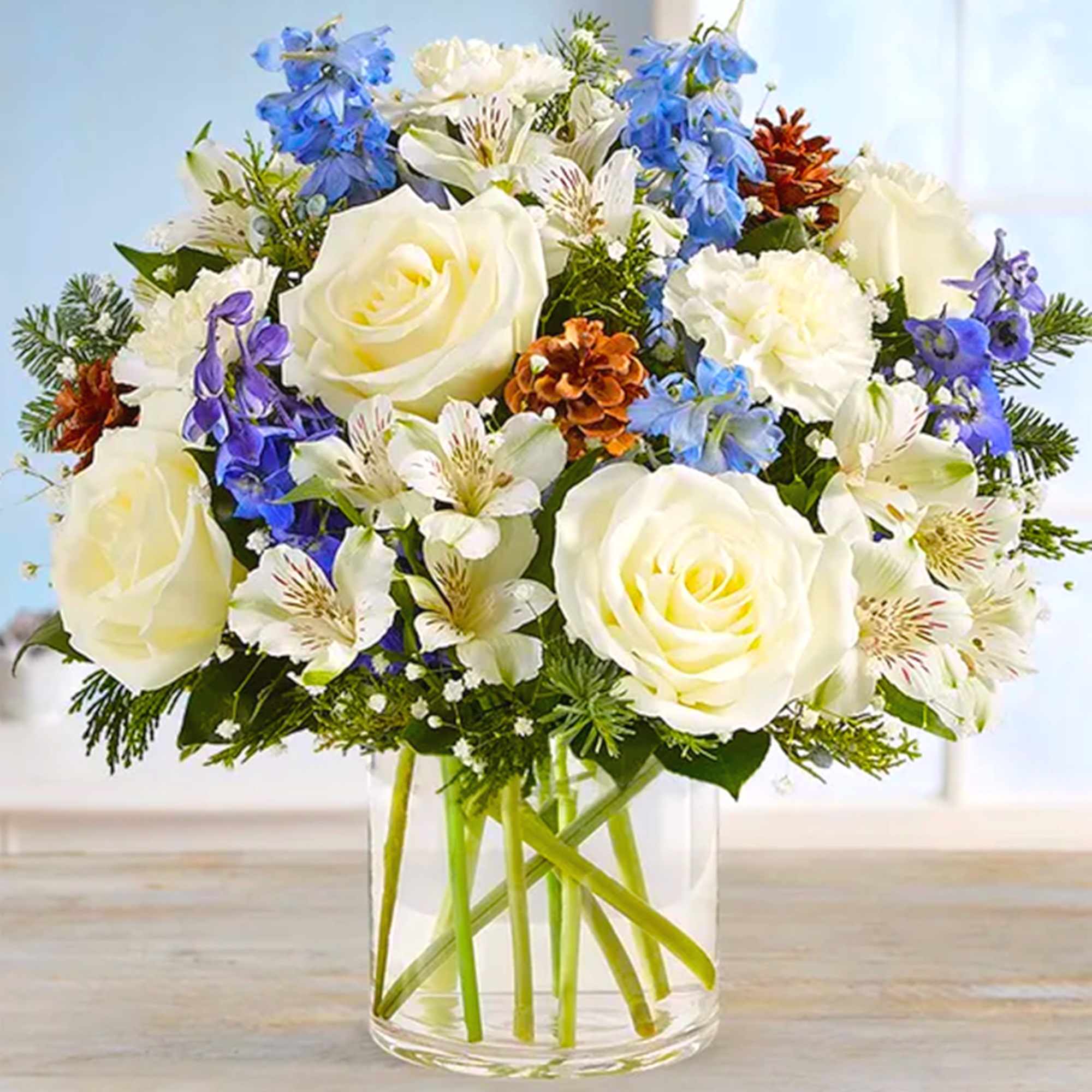 Bouquet of white roses, blue flowers, and white lilies in a clear glass vase