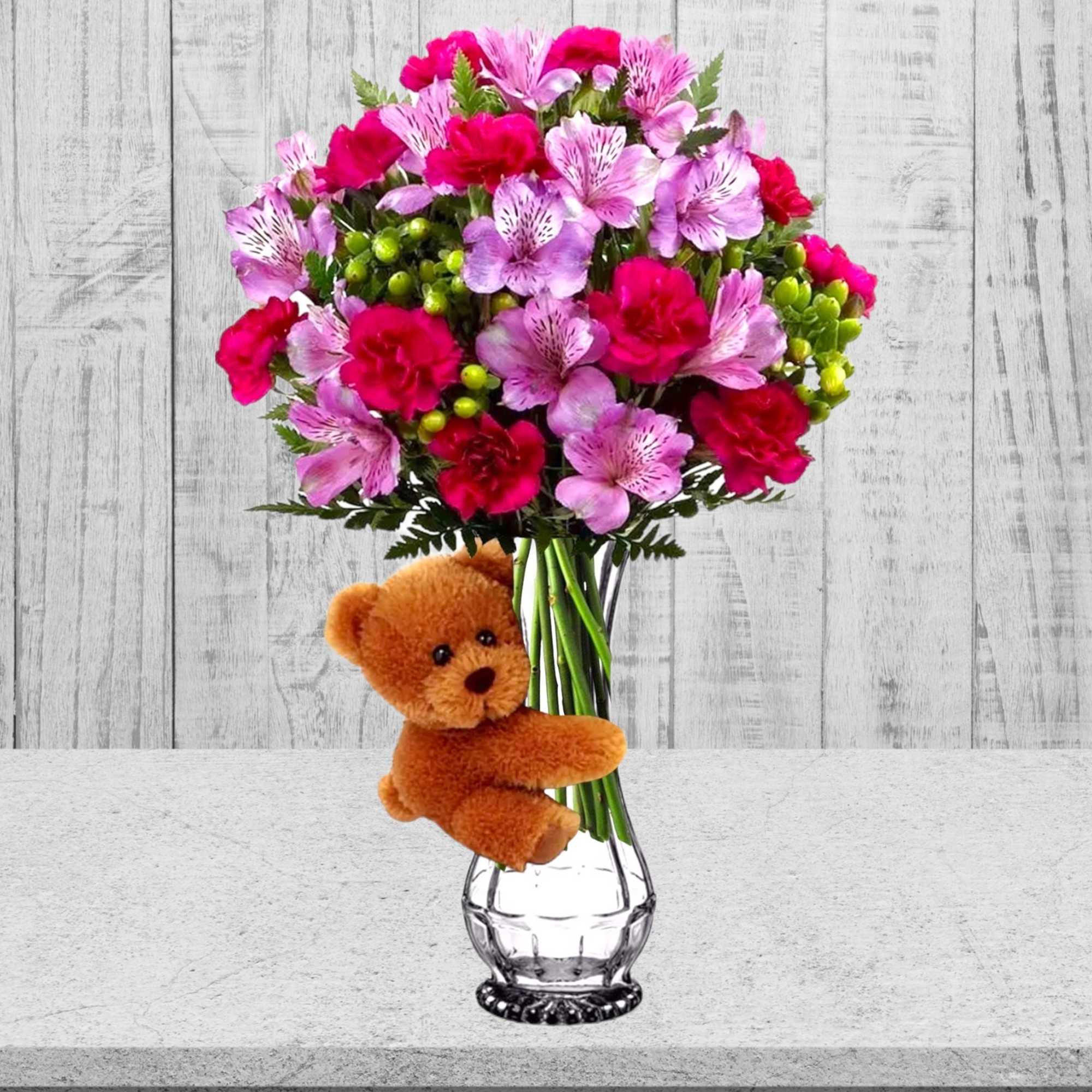 Pink and magenta bouquet in a clear vase with a teddy bear attached