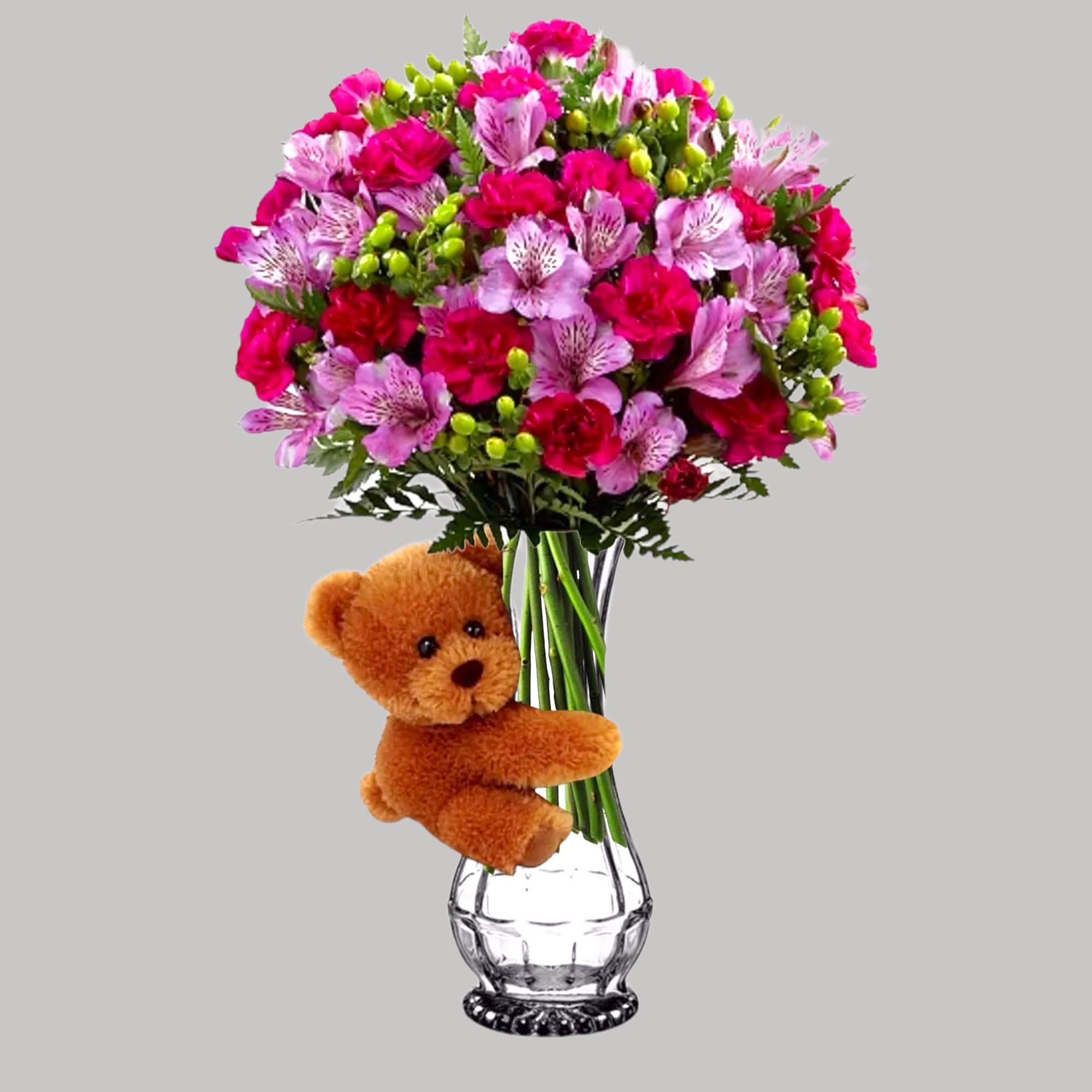 Pink and red bouquet in a glass vase with a teddy bear attached