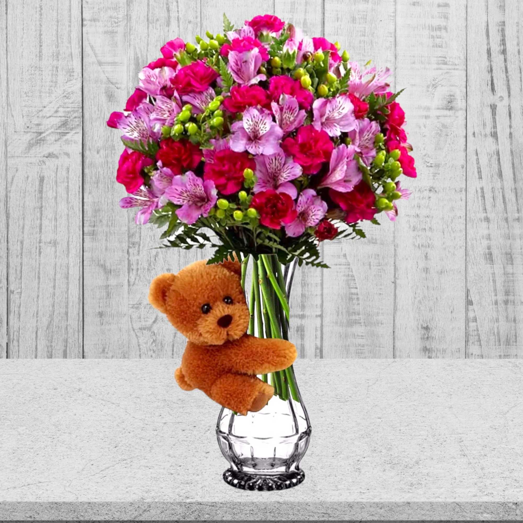 Pink and magenta bouquet in a clear glass vase with a teddy bear