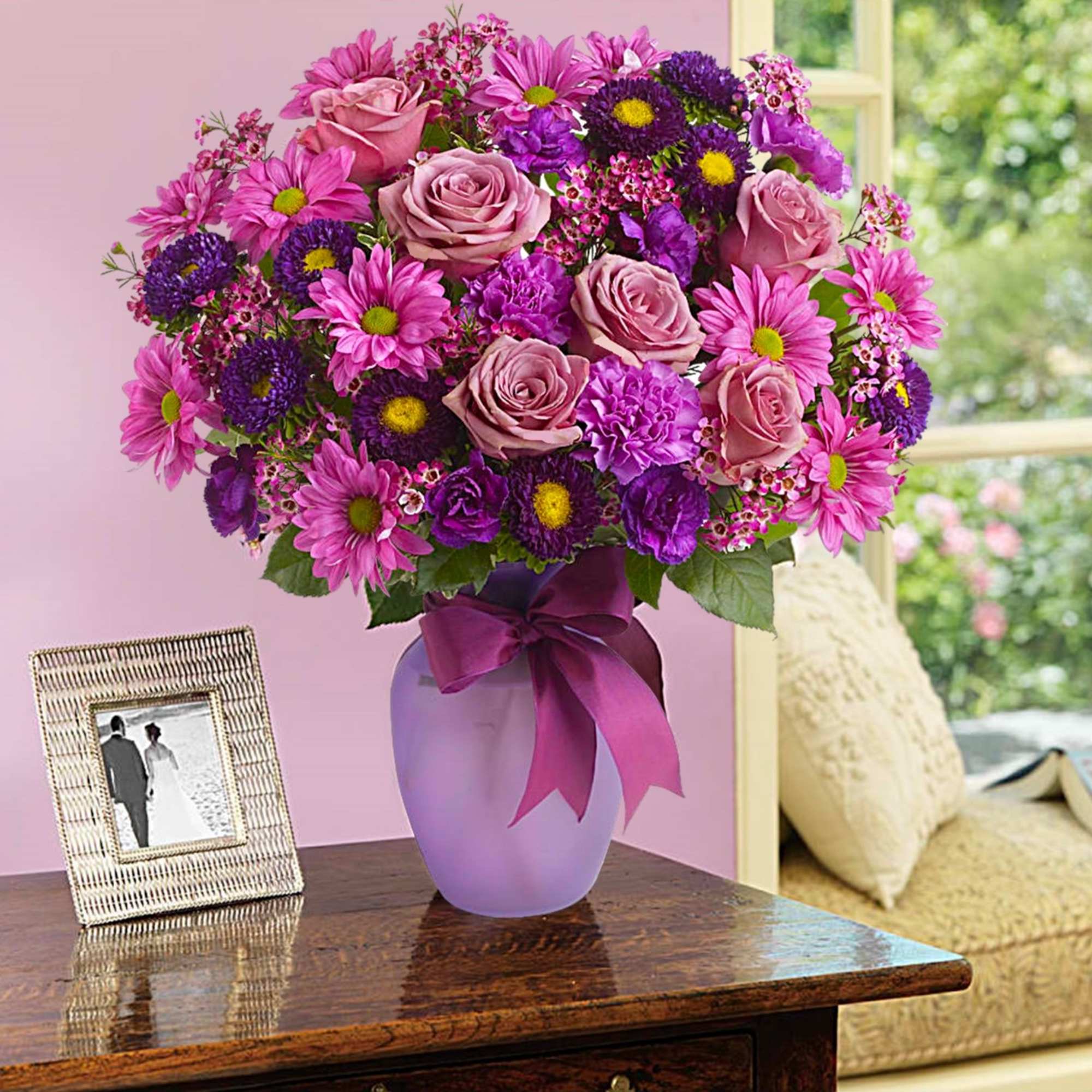 Pink and purple mixed flower arrangement in a lavender vase with a ribbon