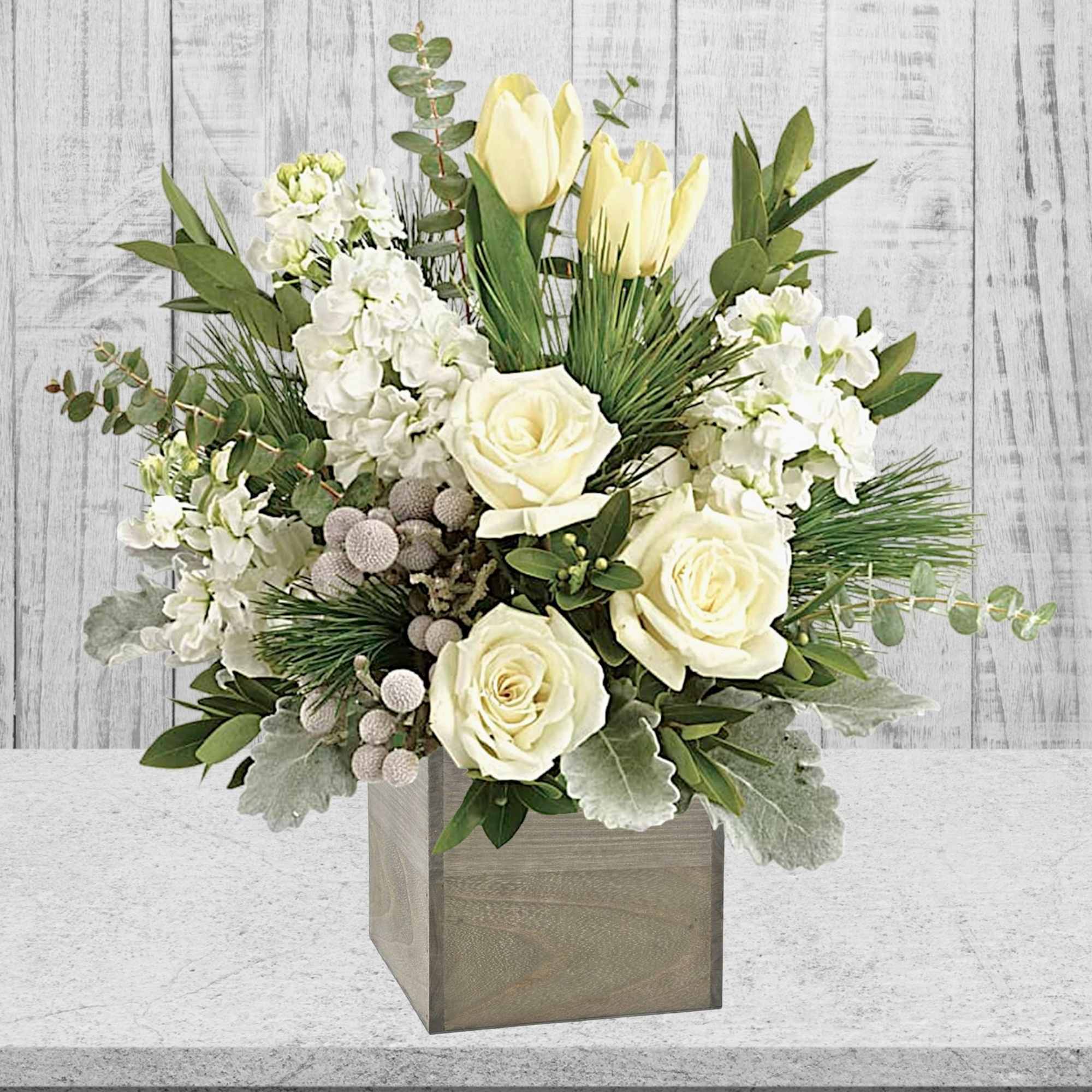 White roses and pale yellow tulips in a square vase with greenery