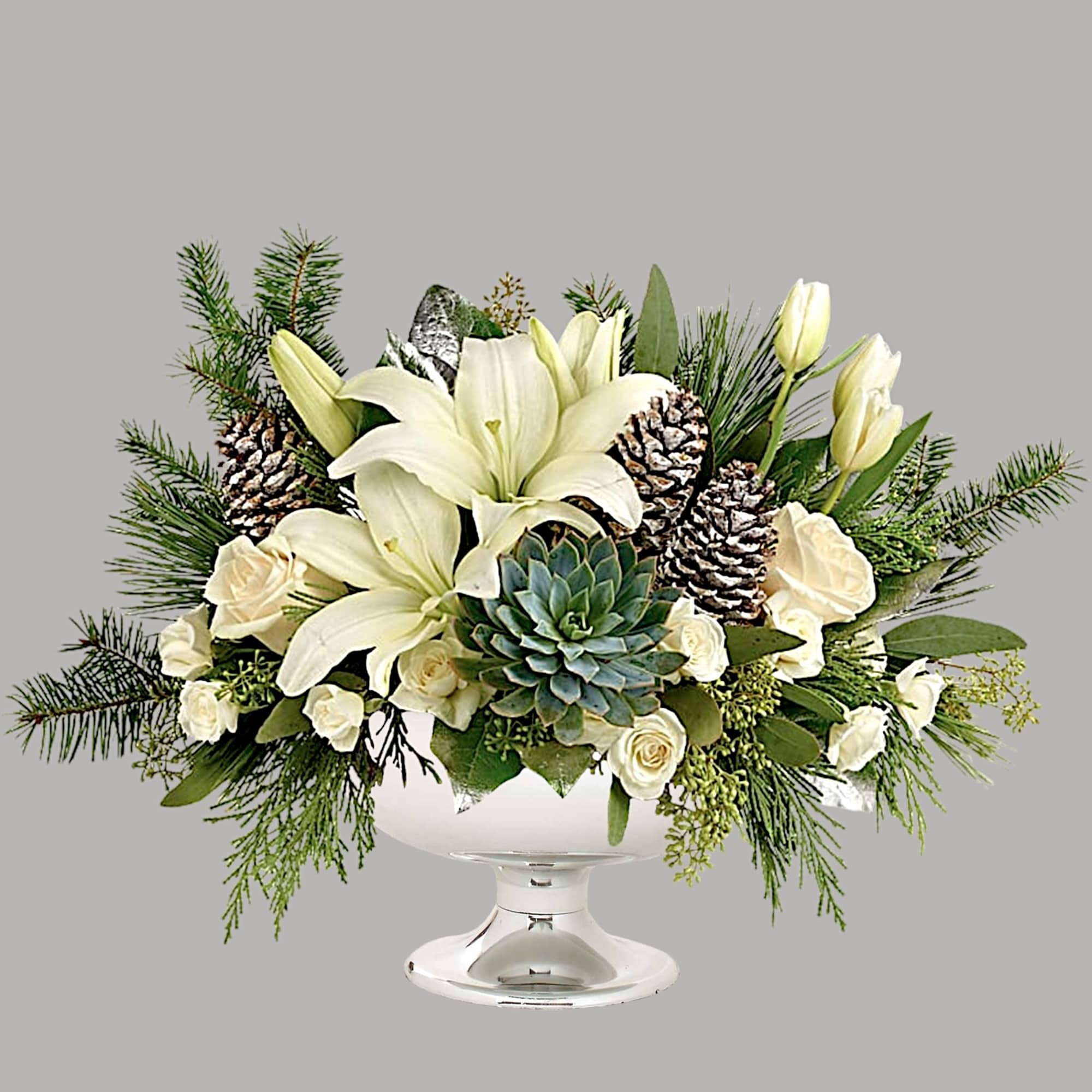 White lilies and roses in a glass pedestal vase with pinecones and a succulent