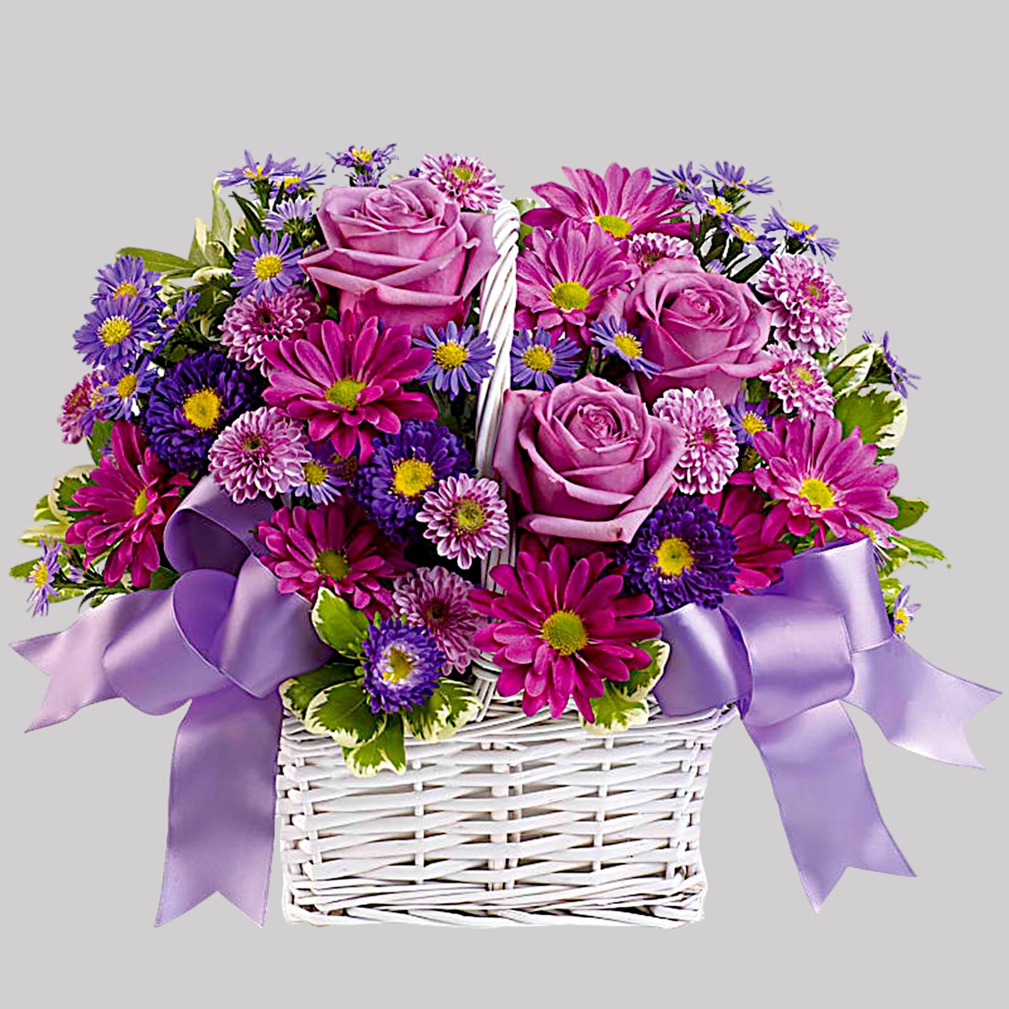 Pink roses and purple daisies in a white wicker basket with lavender ribbon