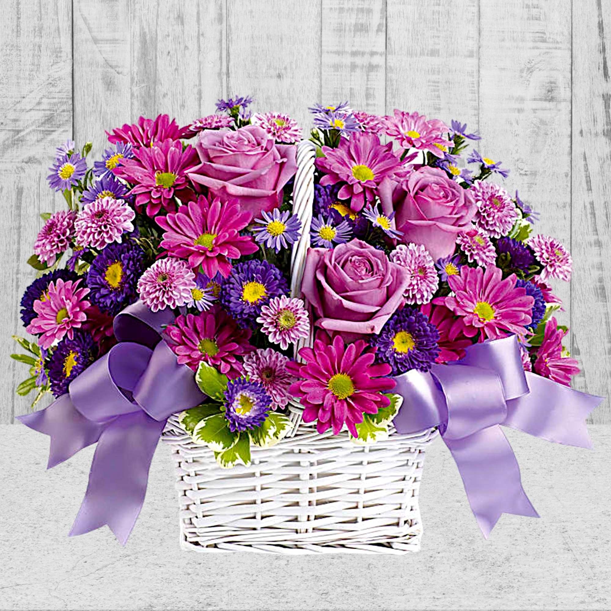 Pink and purple flowers in a white basket with lavender ribbon