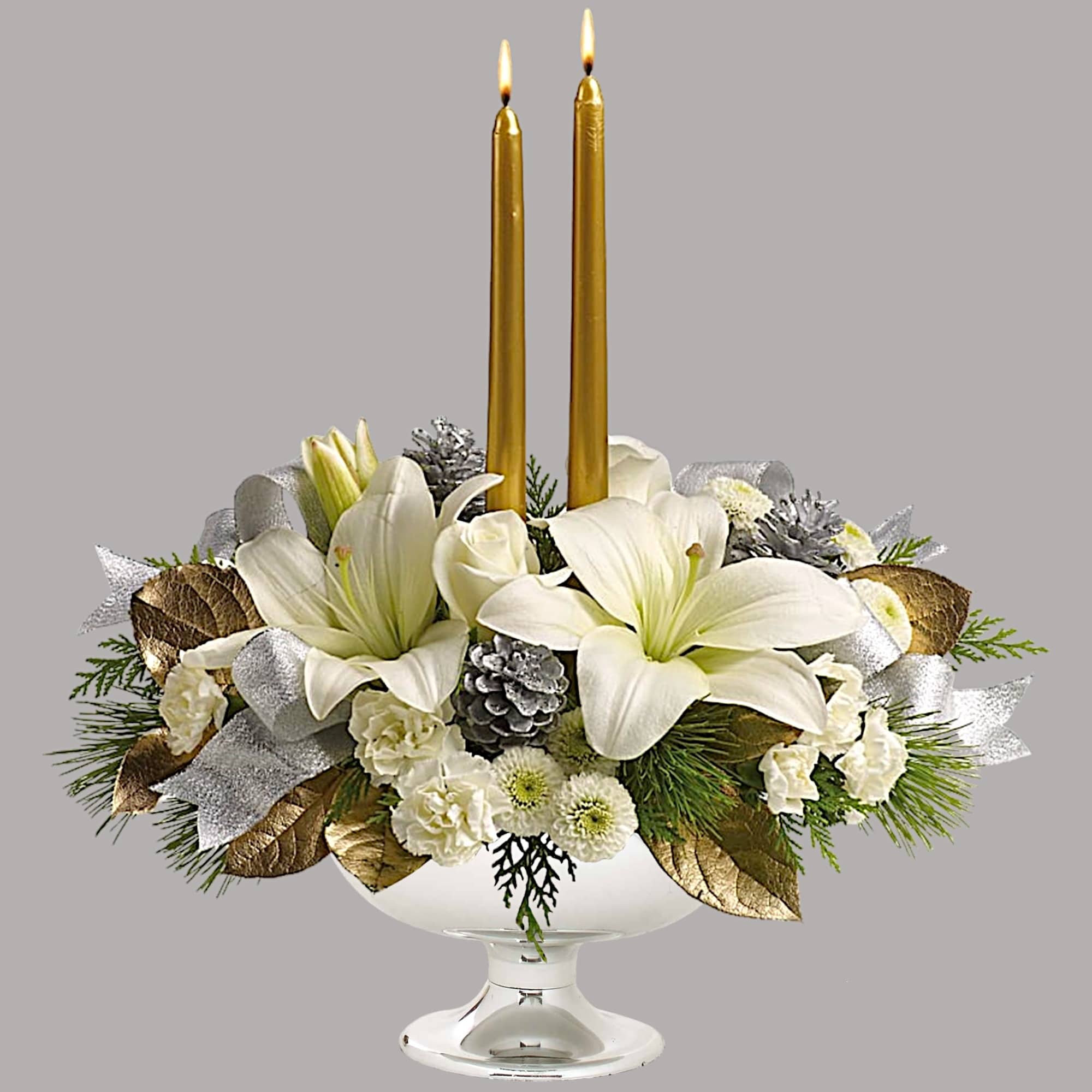 White floral centerpiece with two gold taper candles in a glass compote
