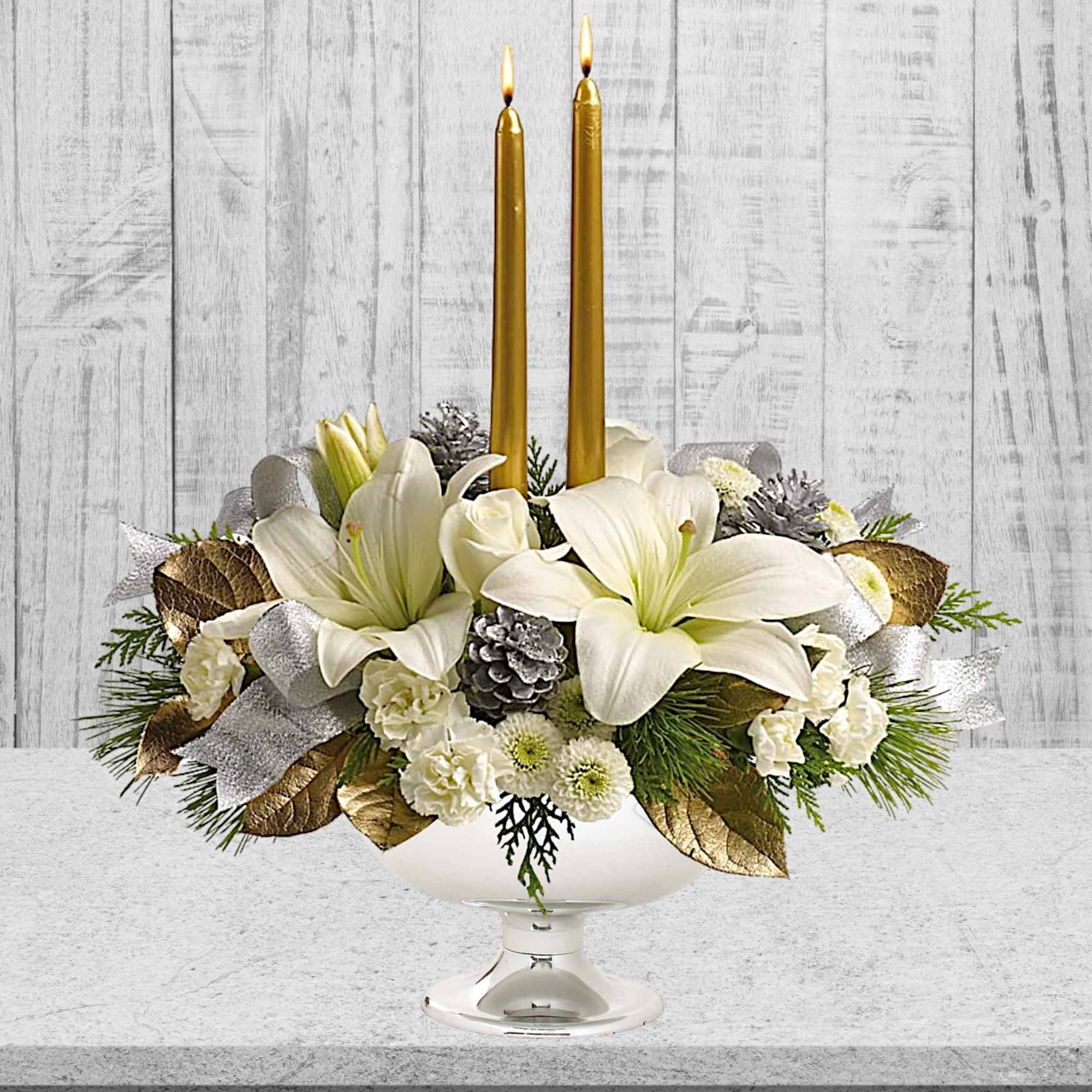 White floral centerpiece with two gold taper candles in a glass pedestal bowl