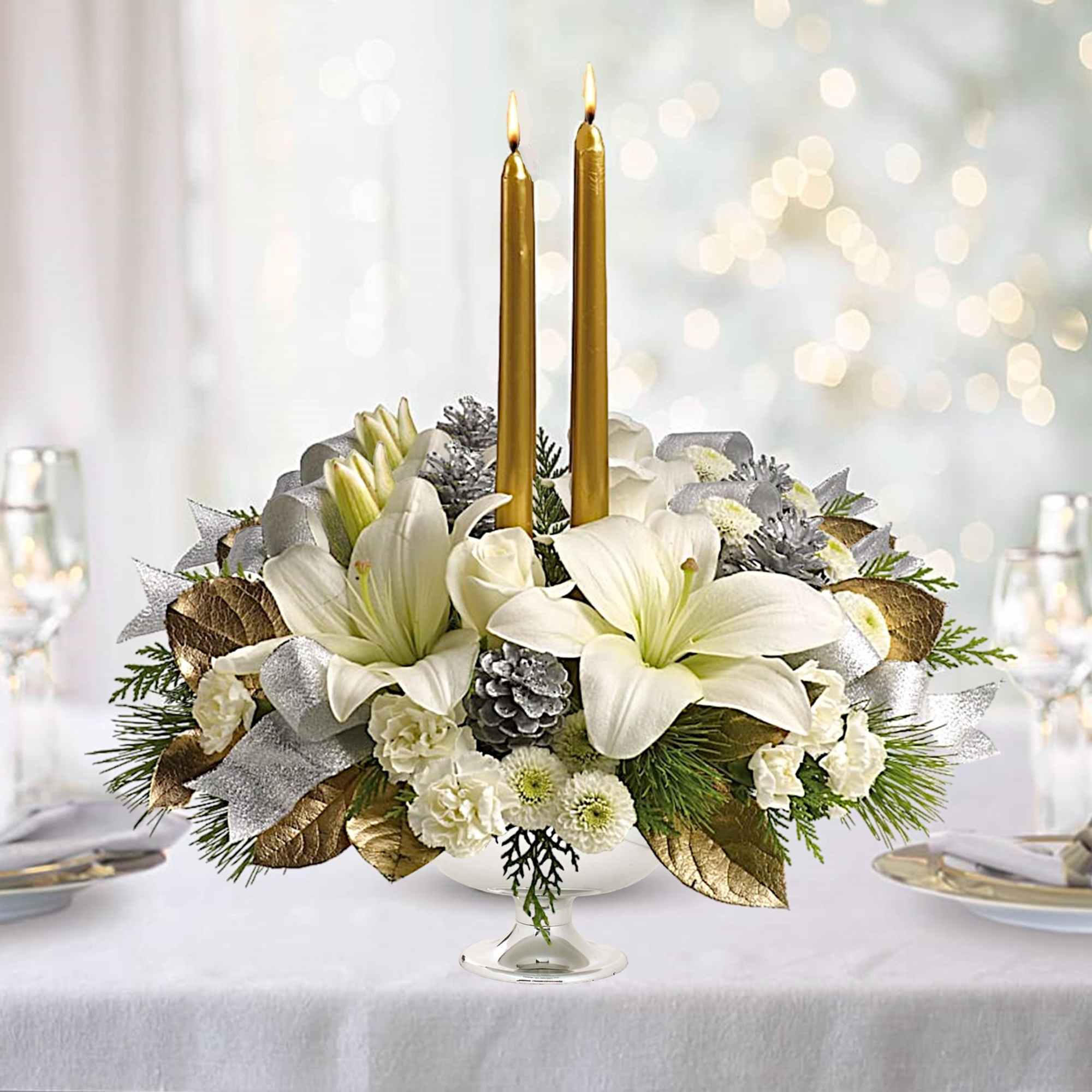 White floral centerpiece with two gold taper candles in a glass pedestal vase