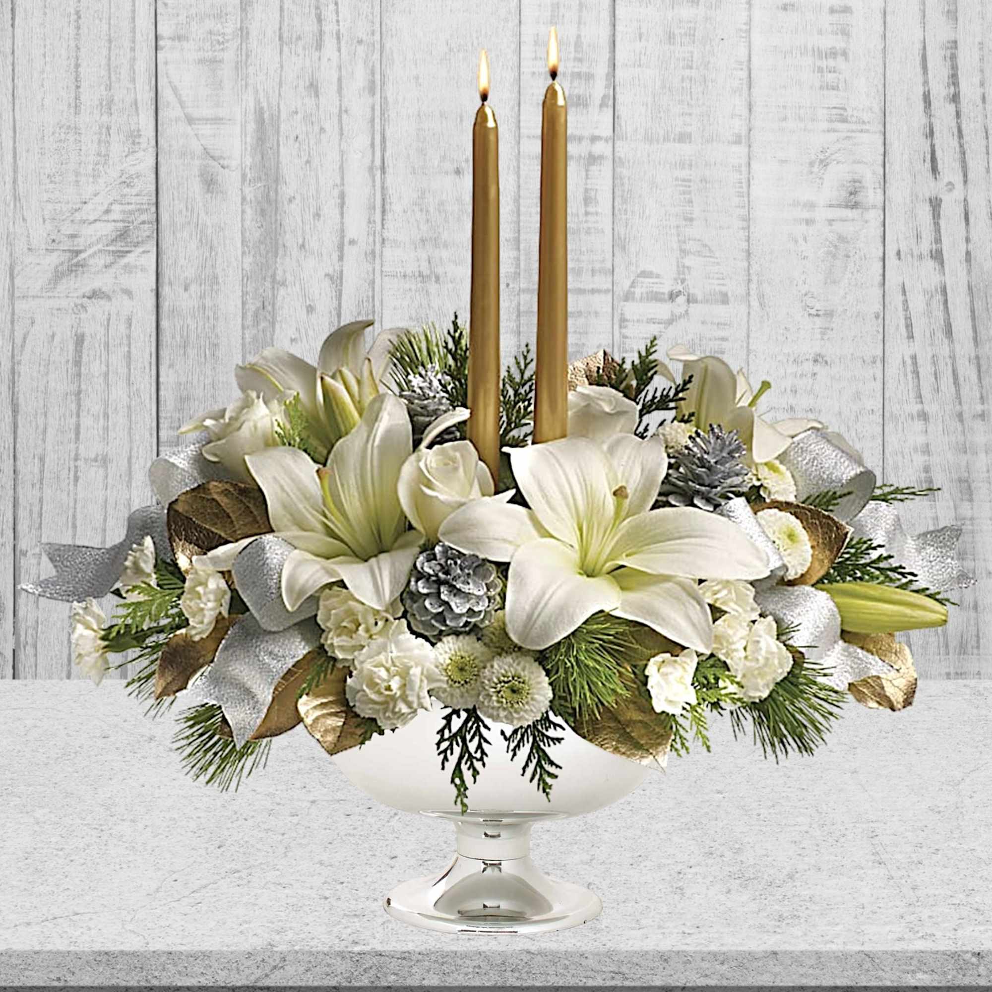 White floral centerpiece with two gold taper candles in a silver bowl vase