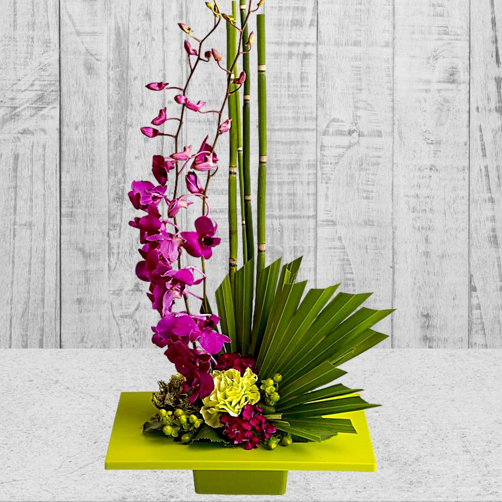 Magenta orchid arrangement with bamboo and fan leaves in a lime green container