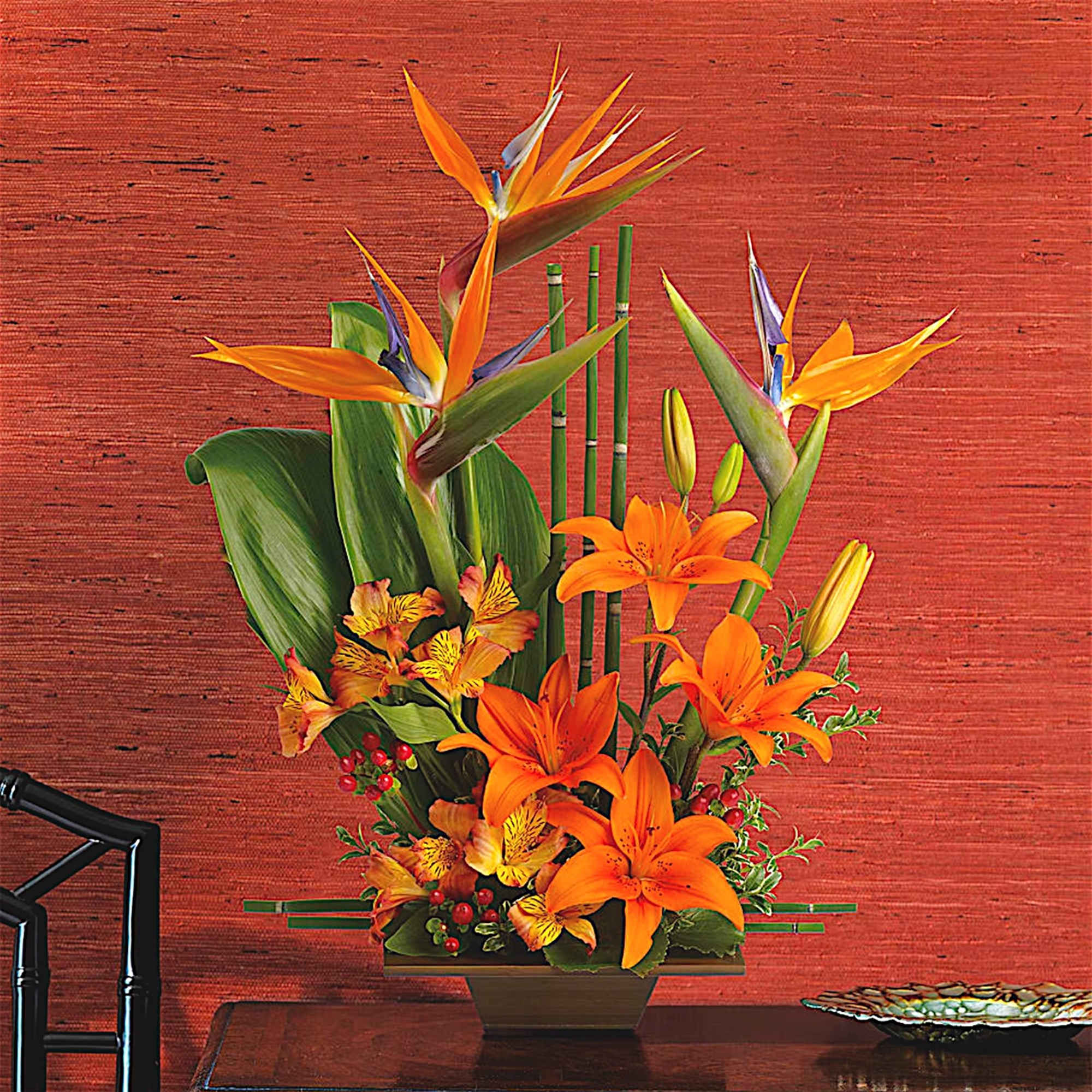 Orange lilies and bird of paradise in a square vase
