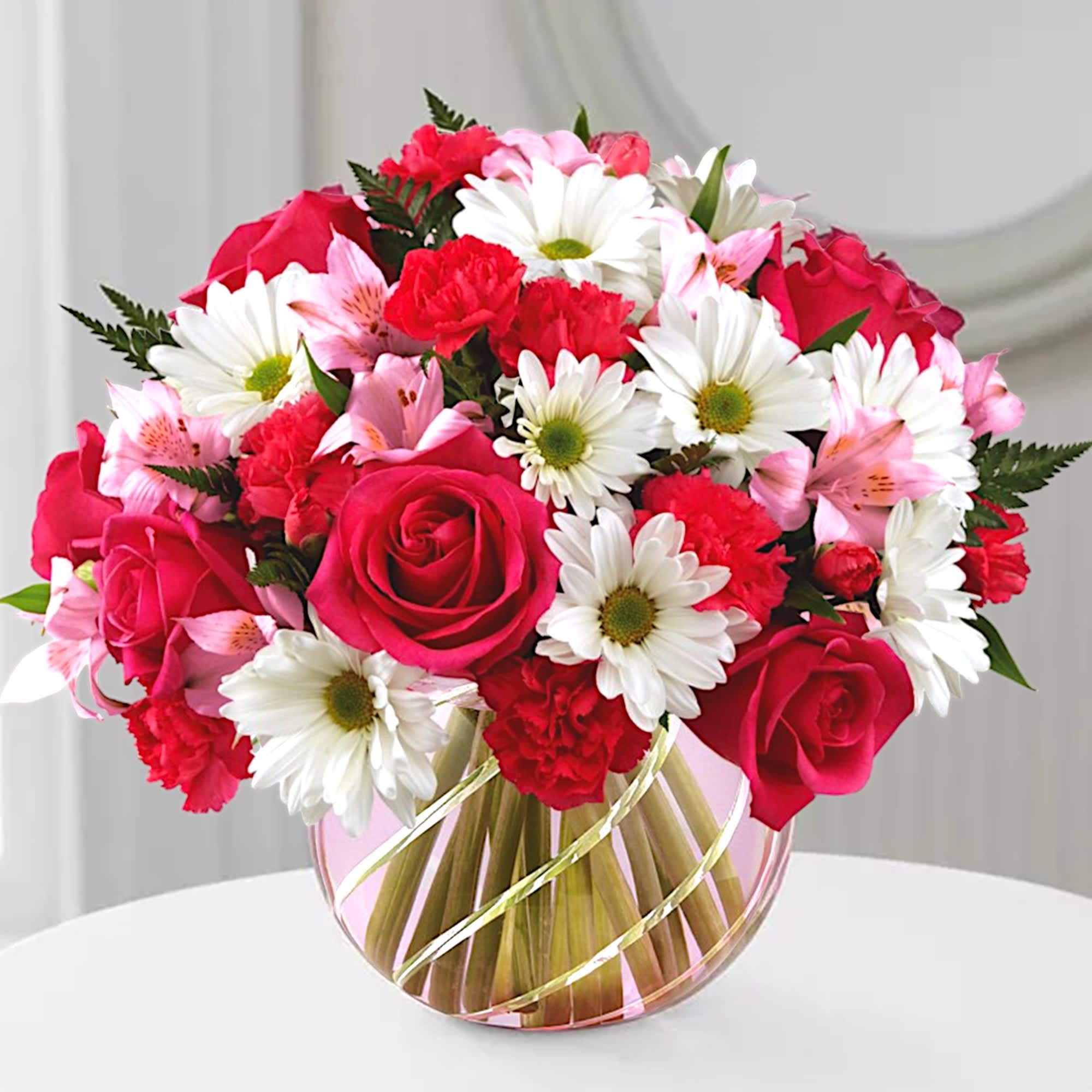 Bouquet of red roses, white daisies, and pink lilies in a round glass vase